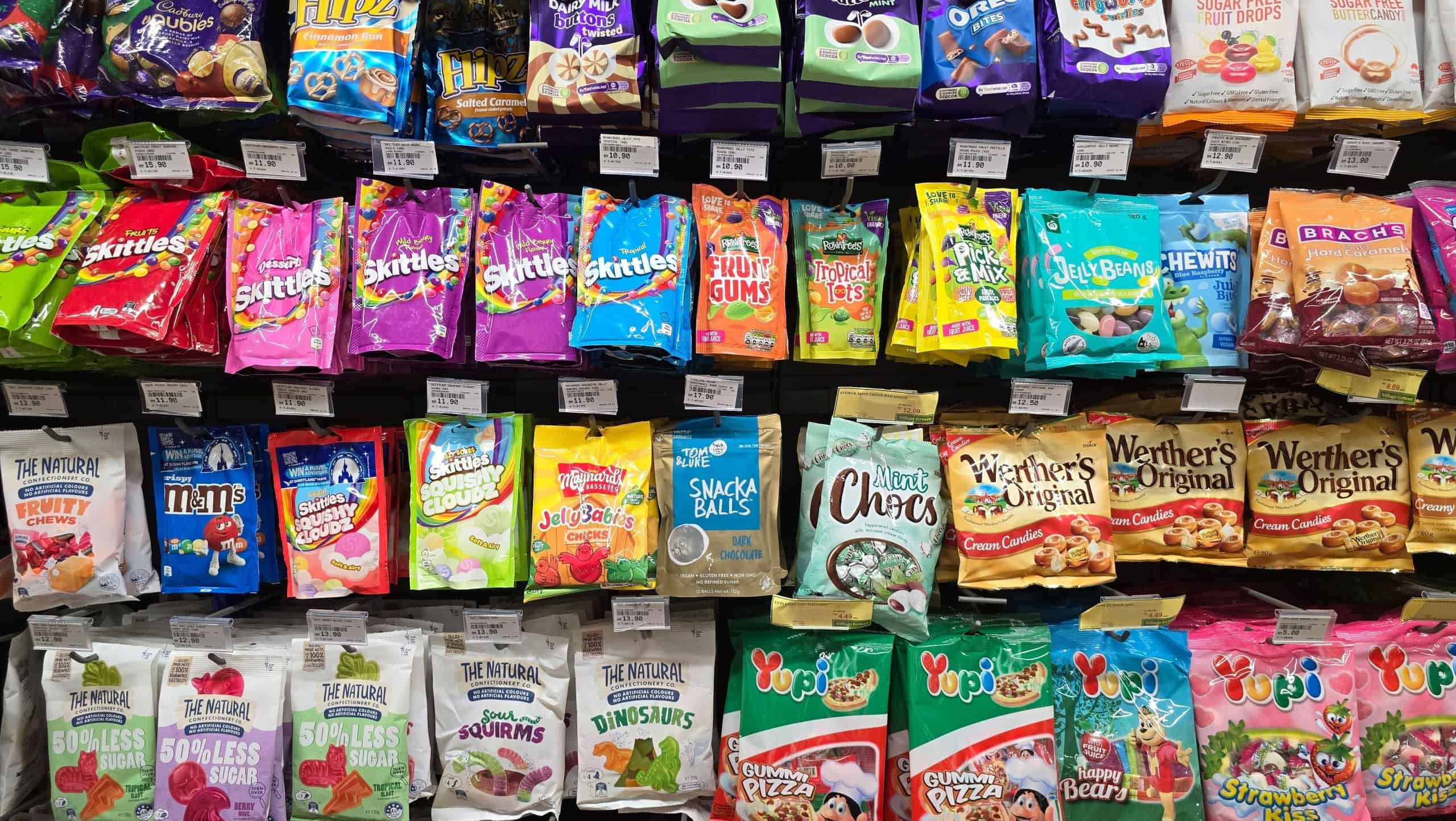Bangsar, Malaysia – Mar 29, 2025: Bright and colorful assortment of candies including Skittles, MM's, gummies, and sugar-free treats neatly arranged on a shelf at a supermarket.