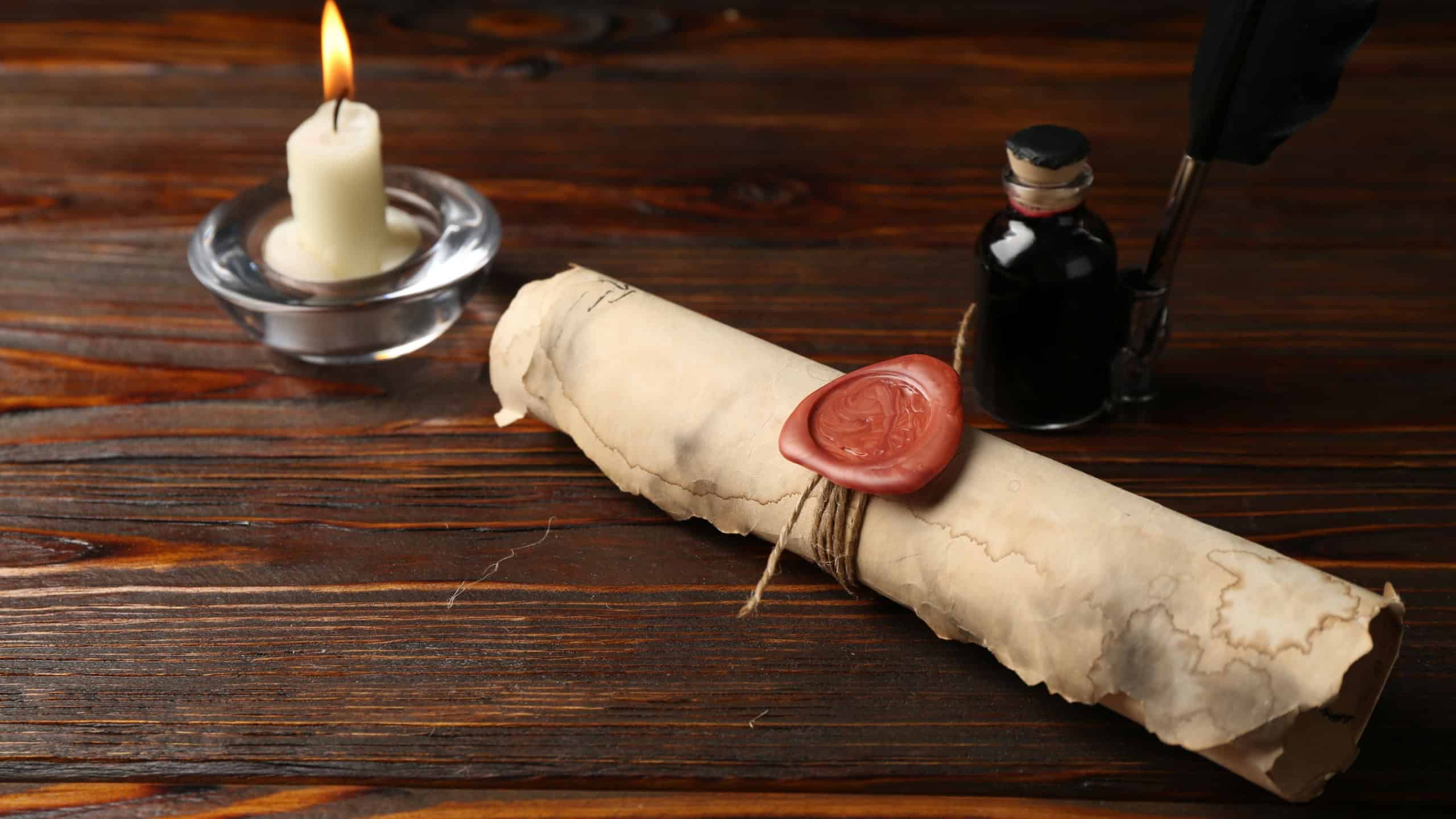 Old rolled scroll, burning candle, feather and inkwell on wooden table
