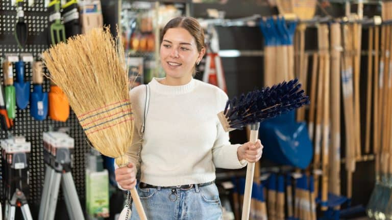 European woman chooses a large broom and a brush for the garden. Customer on sale in a garden store for the summer season