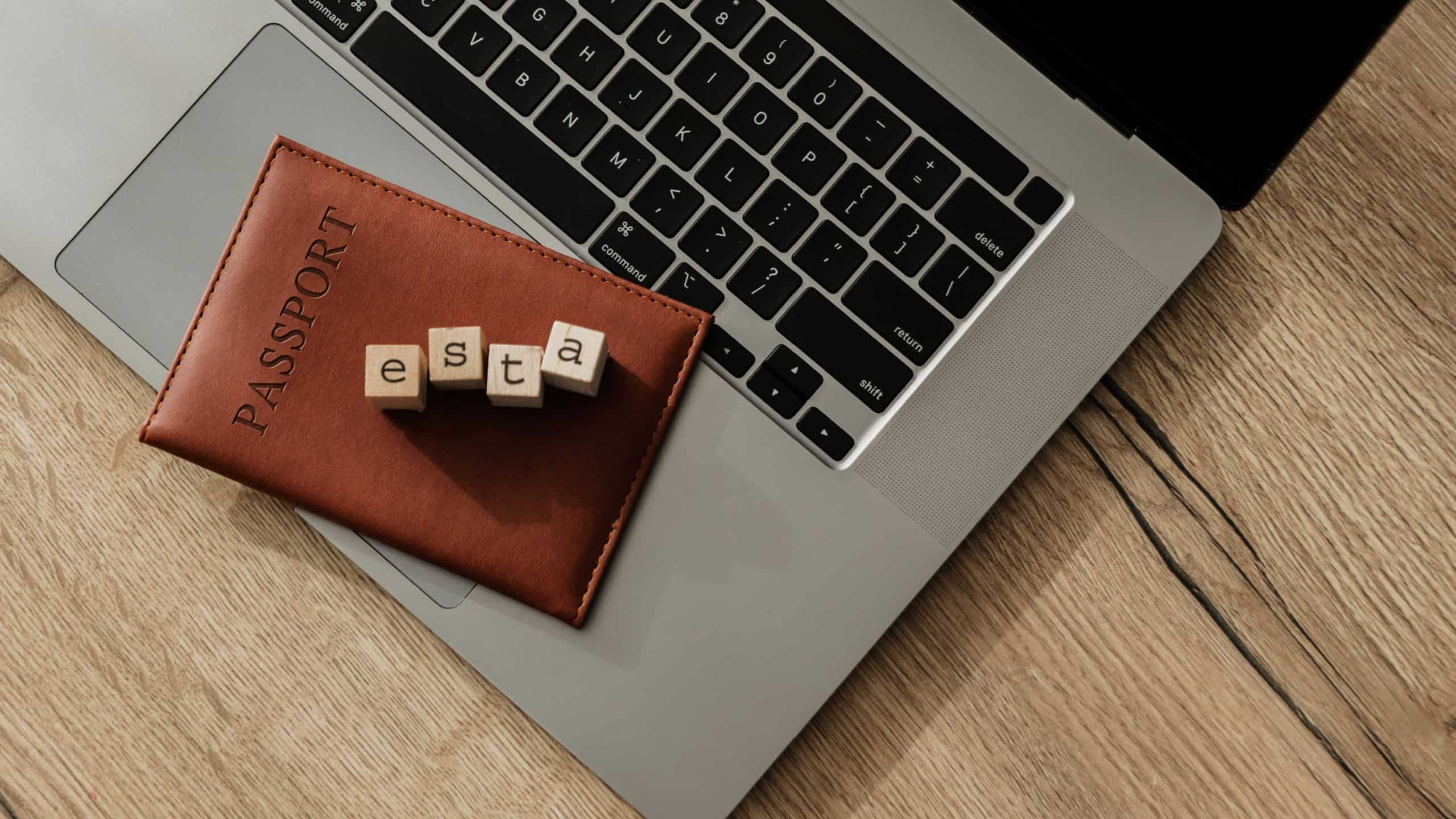 Wooden blocks spelling “ESTA” placed on a passport over a laptop keyboard, symbolizing electronic travel authorization to the United States.