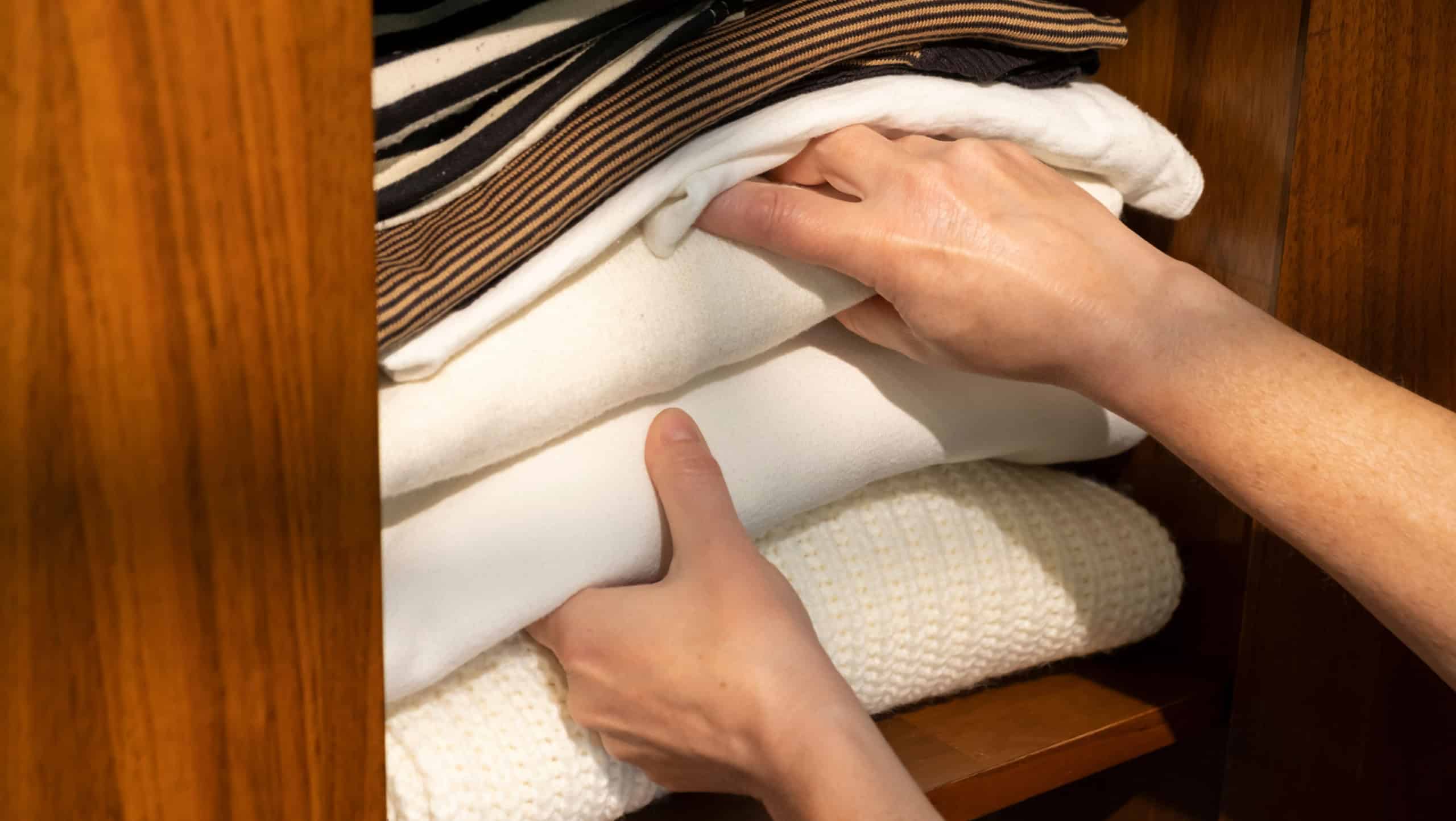 Organizing and folding clothes neatly in a wooden cabinet during a tidy-up session at home