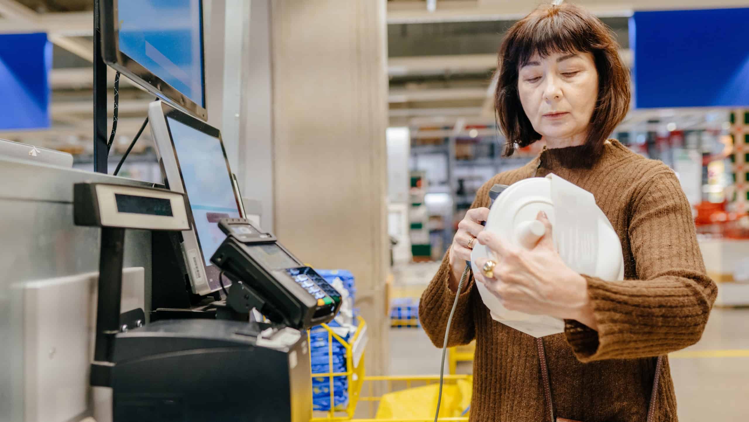 Mature woman over 55 using barcode scanner at furniture store checkout. Concept of digital skills, self sufficiency, sustainability and active senior lifestyle.
