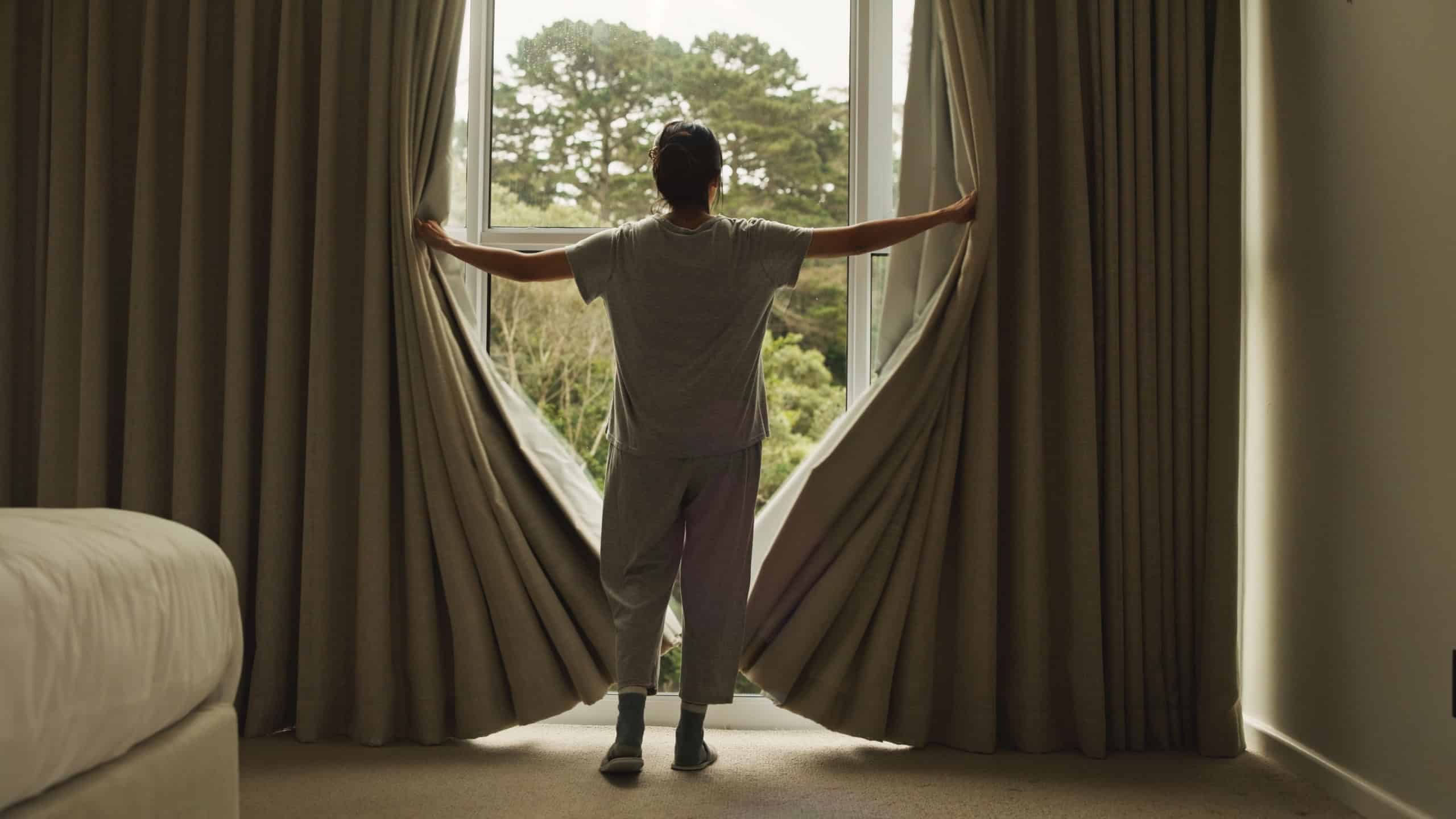 Wake up, curtain and back of woman in hotel room for morning routine, accommodation getaway and relax. Window, hospitality and view with person in house rental for comfortable, trip and sunrise