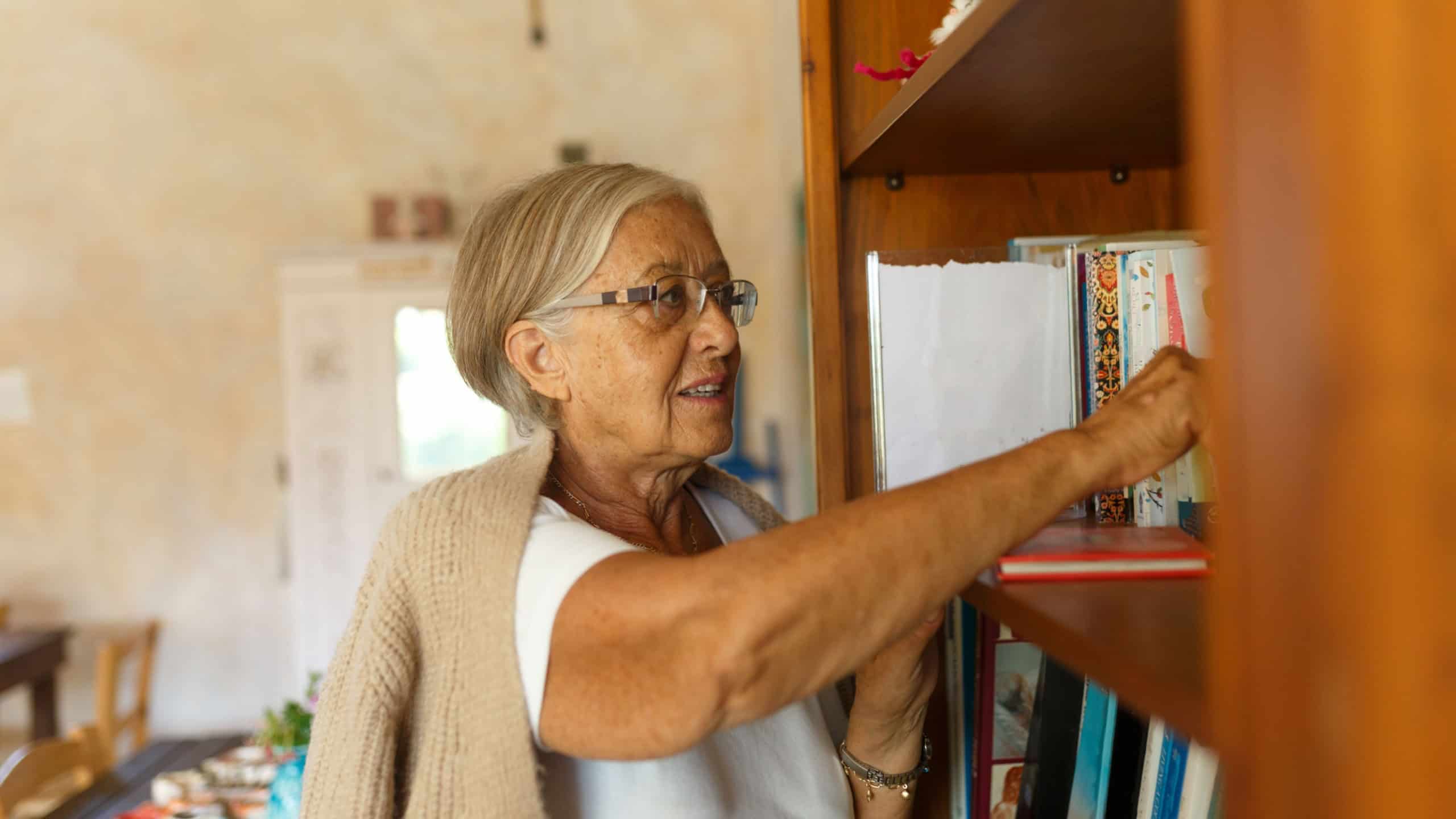 Older woman selecting a book from her home bookshelf, enjoying reading and knowledge