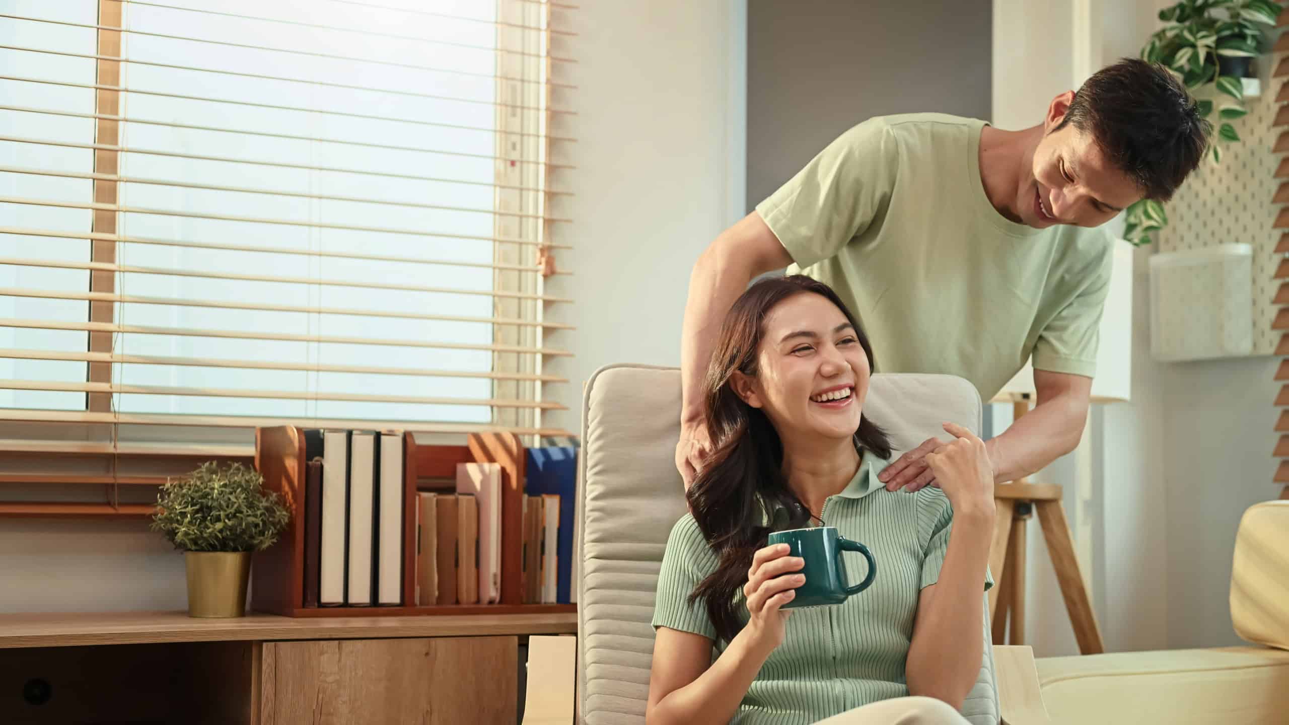 Loving couple relaxing at home, man giving gentle shoulder massage to his smiling partner.