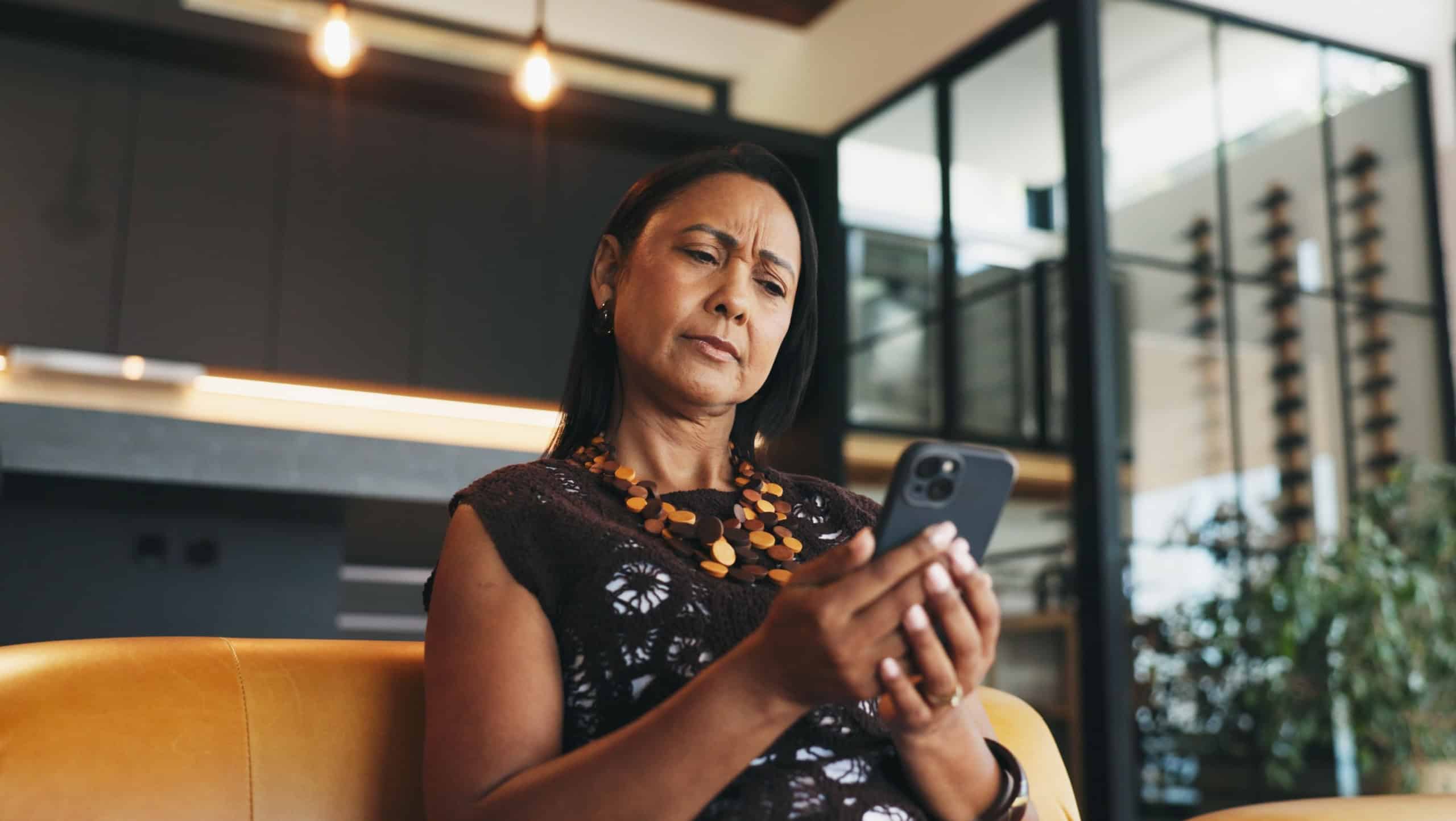 Confused, woman and doubt in home with phone, unexpected news and text message for online gossip. Mature person, concern and reading in house with tech, mobile chat and update for social media rumor.