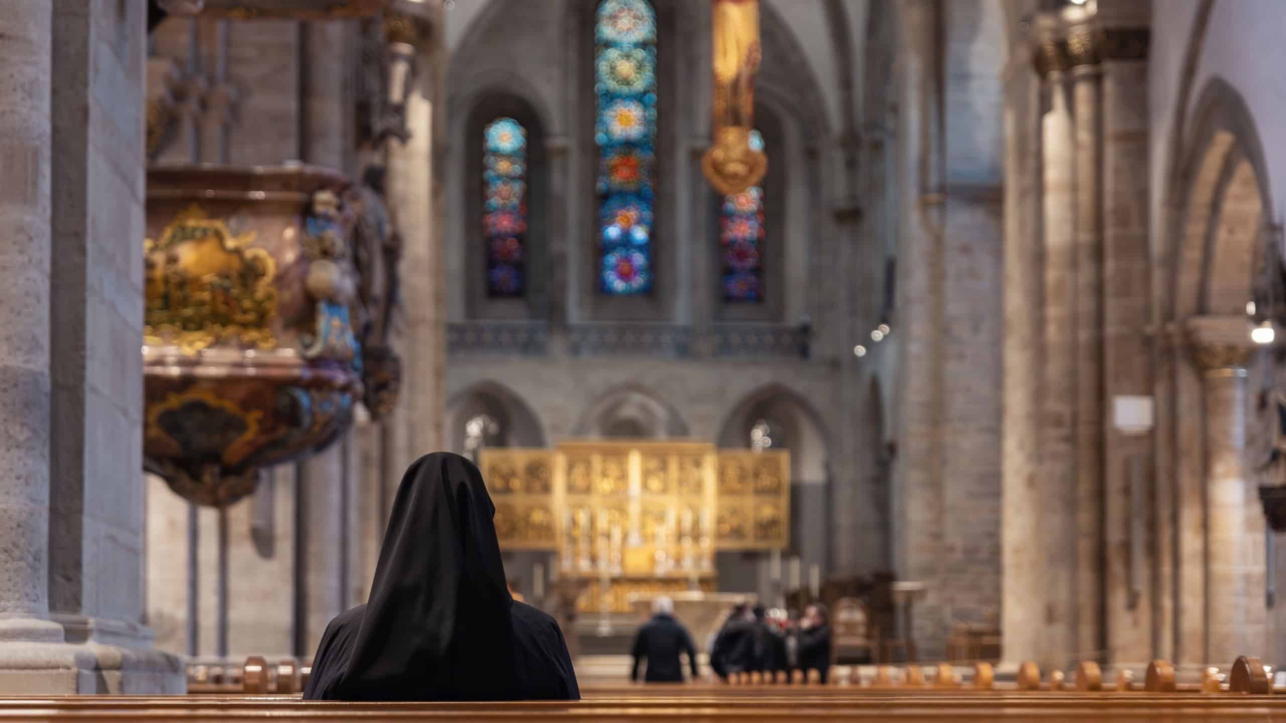 Scenic back view nun sit wooden pew facing altar stained glass windows ornate pulpit religious interior historic European church nave background. Sacred architecture spiritual atmosphere devotion.