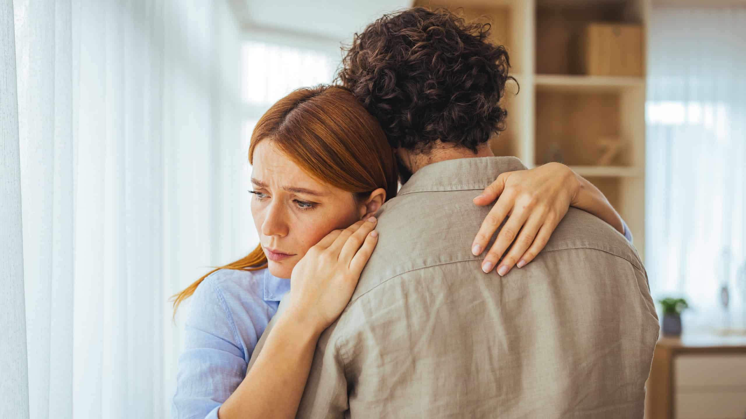 A worried woman embraces her partner for comfort at home, conveying vulnerability, emotional connection, compassion and support during a difficult moment in their relationship.