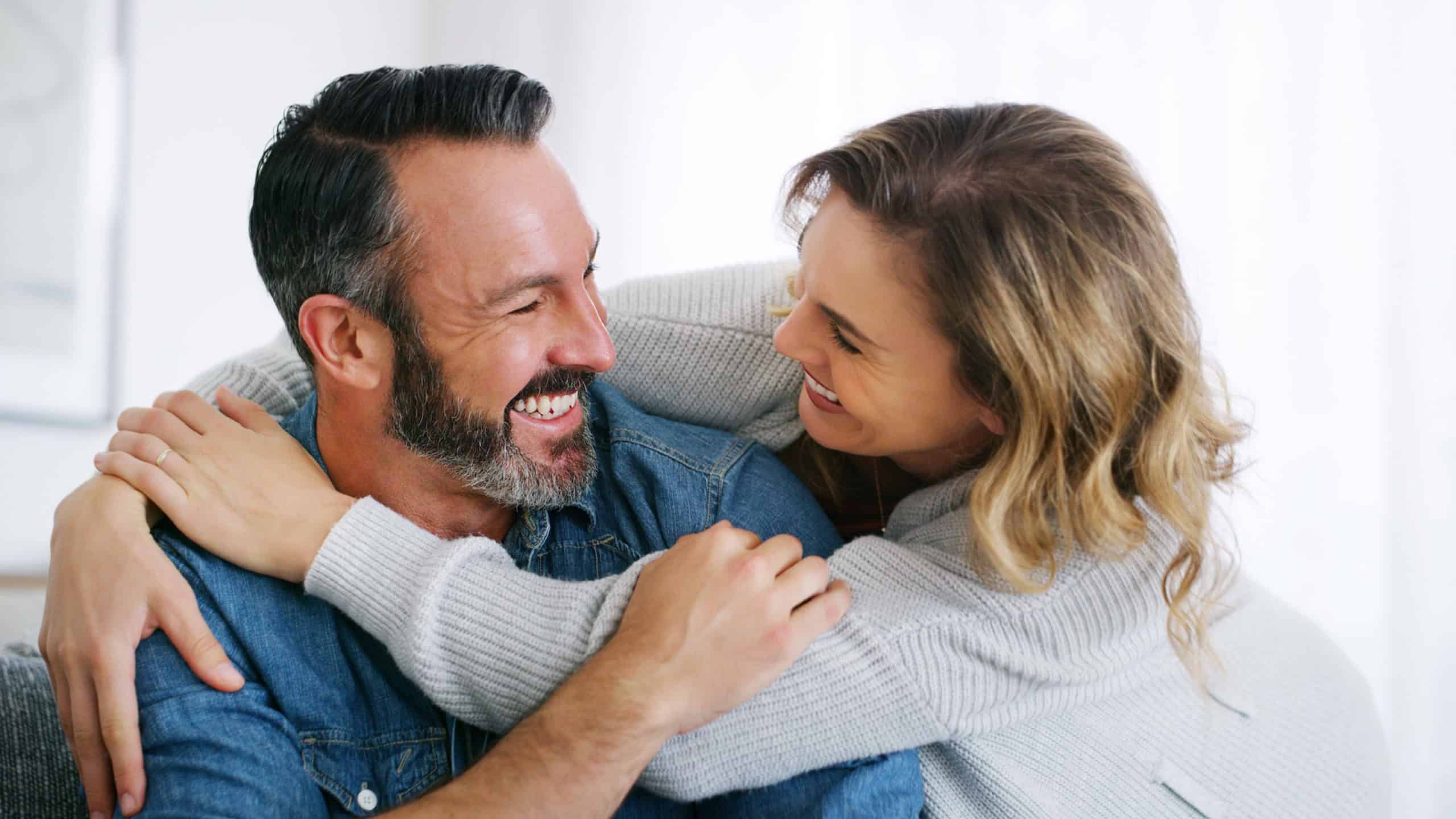 Relax, funny and hug with couple on sofa in home for bonding, connection and support. Weekend break, commitment and laugh with man and woman in living room of apartment for marriage together