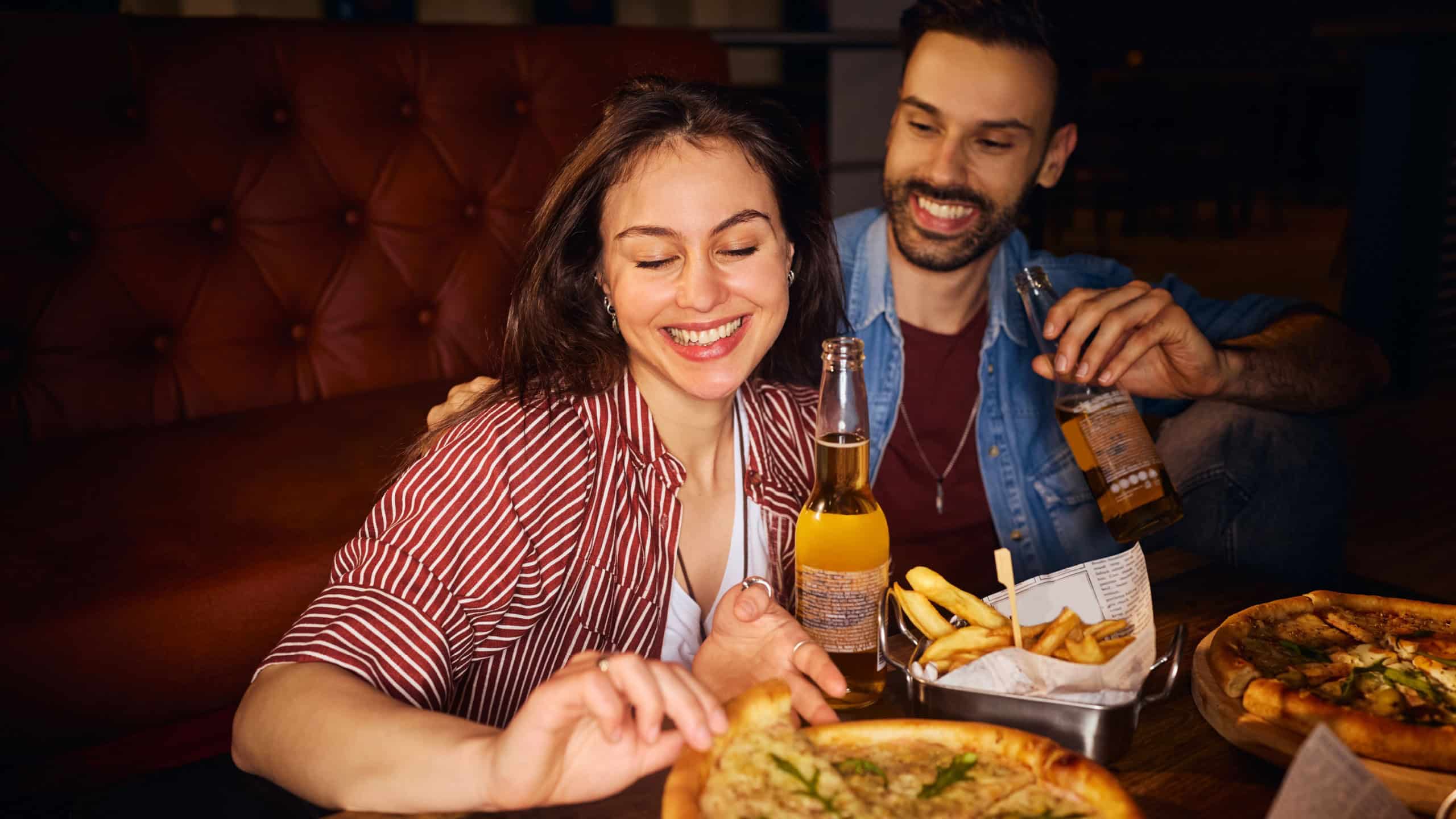 Happy couple enjoying on a date in restaurant. Focus is on woman eating pizza.
