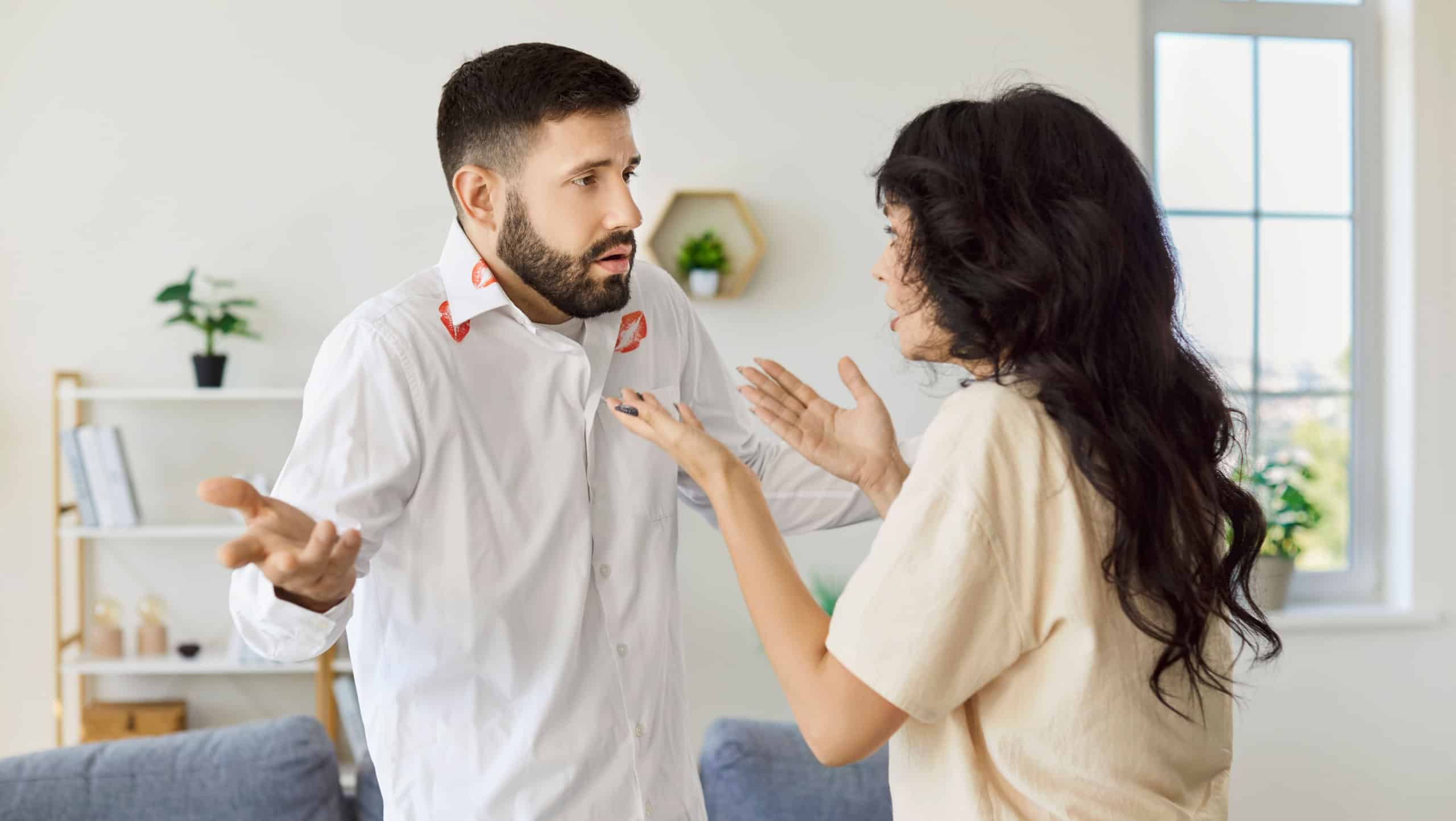 Couple argument about infidelity and lipstick stains. In living room, she challenges him about marks on his shirt he looks guilty and confused. Family relationship conflict and betrayal.