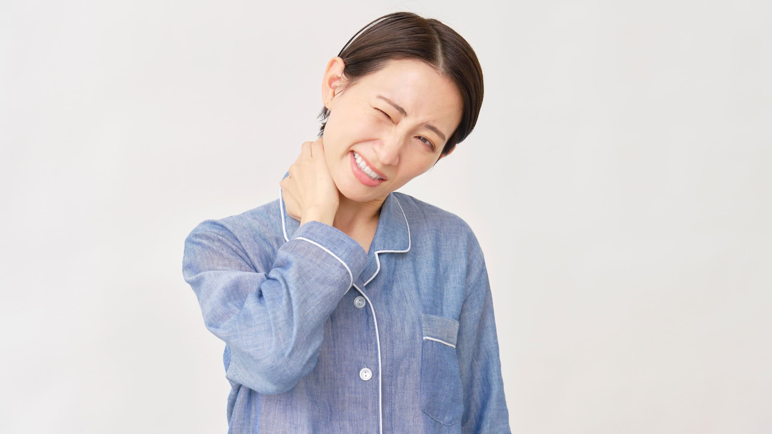 Asian woman in pajamas with stiff neck pain on white background