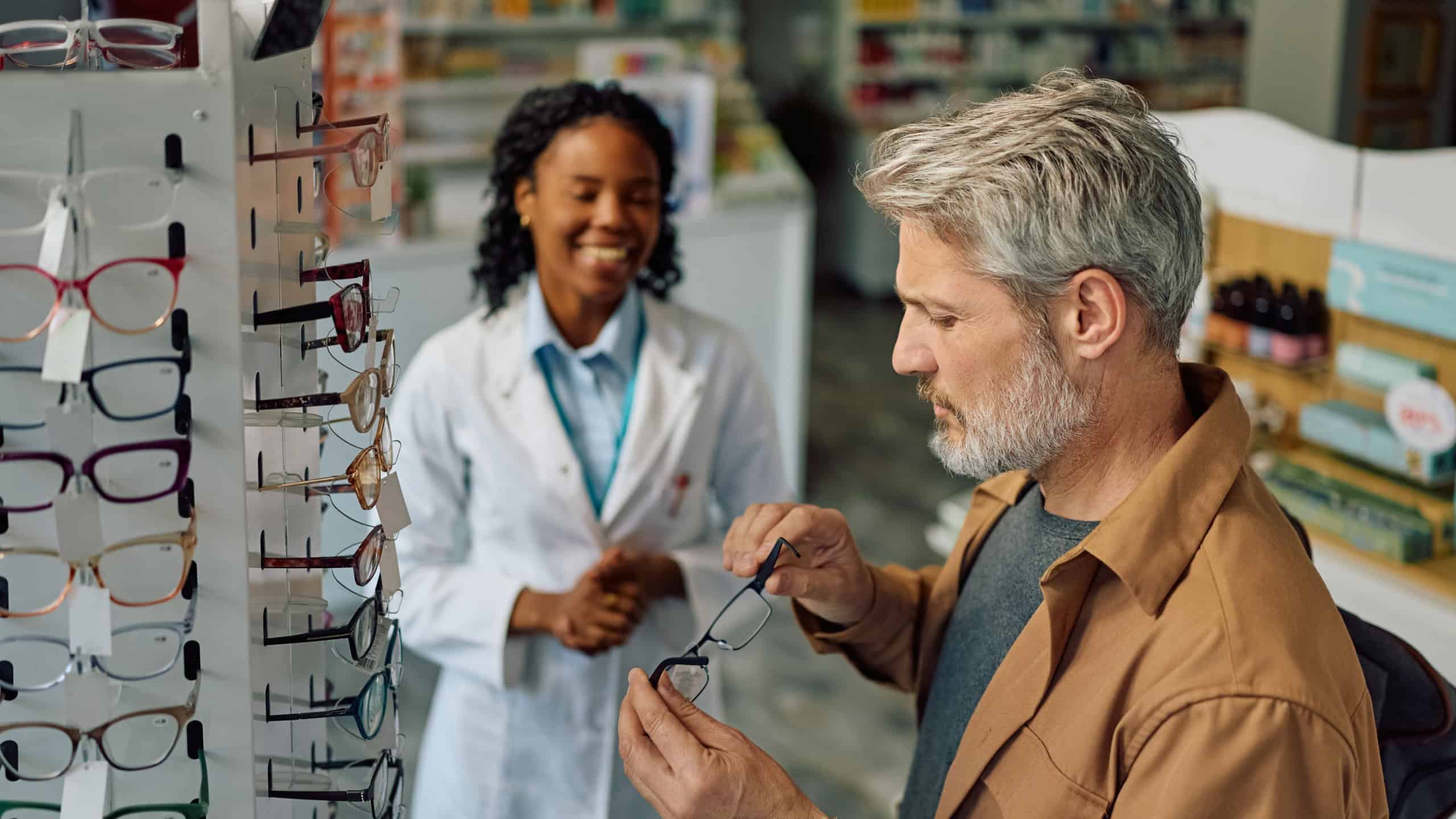 Mature man buying new eyewear frame with ophthalmologist's assistance in a pharmacy.
