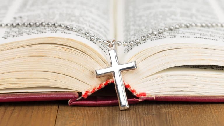 Necklace with silver cross on wooden table and opened bible book