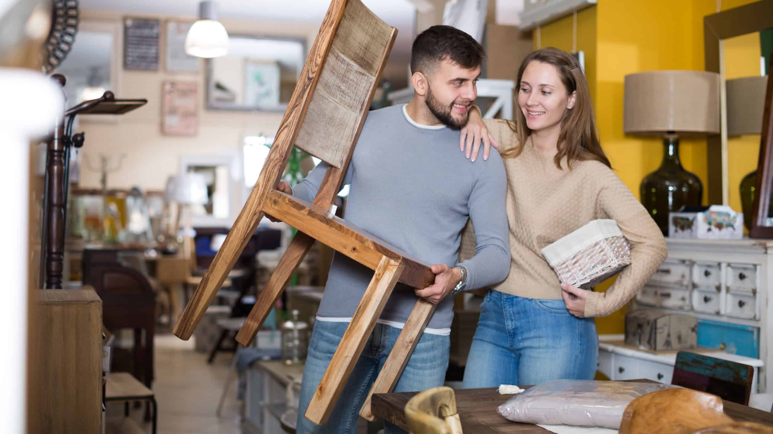 Young woman with boyfriend holding vintage chair in apartment crowded of old furniture