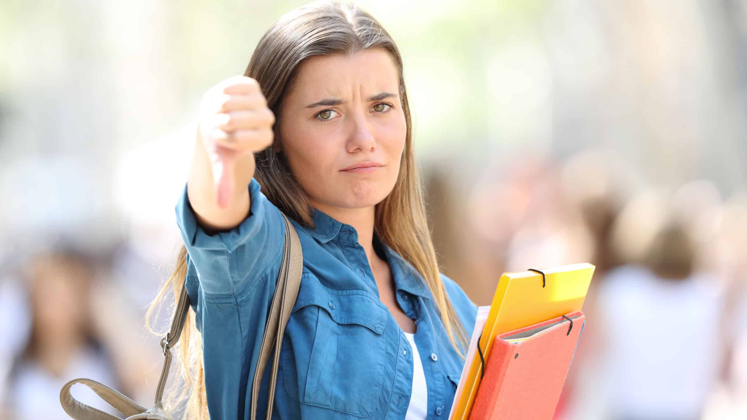 Angry student gesturing thumbs down looking at camera in the street