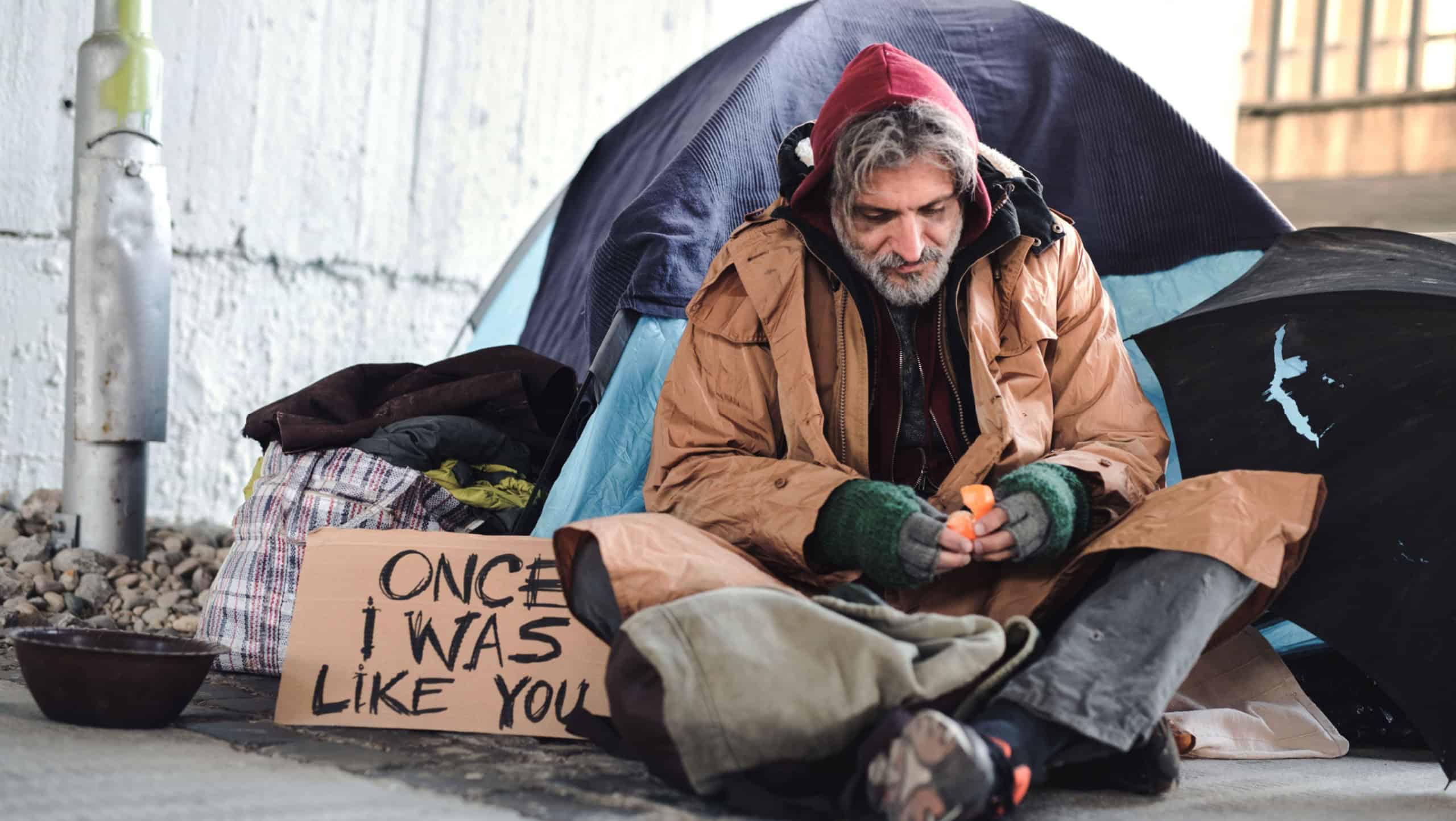 Homeless beggar man sitting outdoors in city asking for money donation.