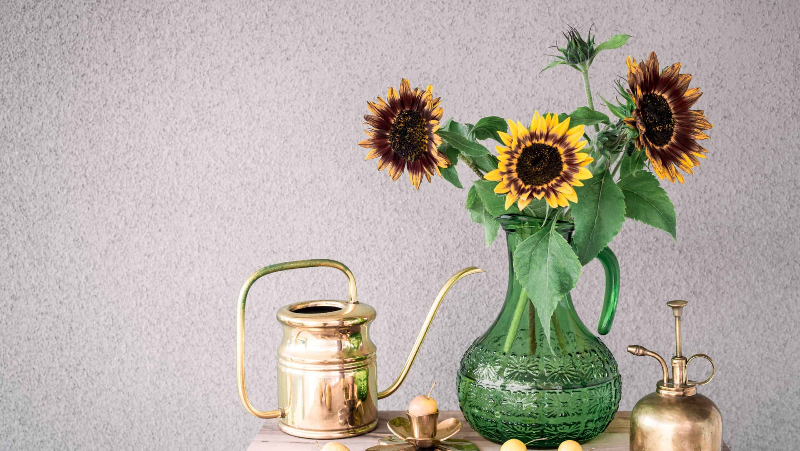 Bouquet of sunflowers in a green glass vase and brass home decor, on concrete background with copy space.