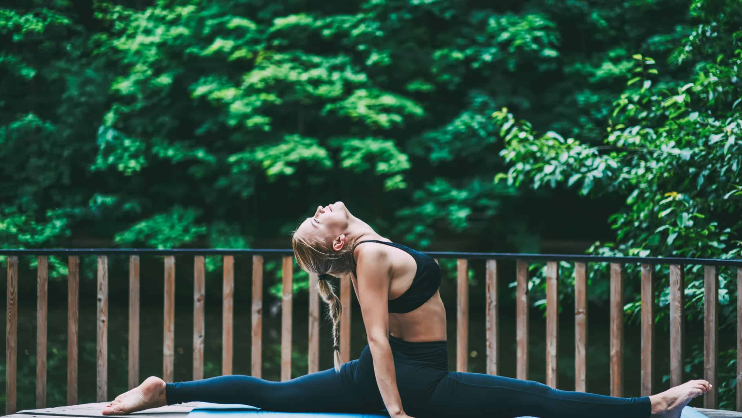 Sportive fitness girl stretching out on mat and looking up during workout, young woman doing exercises to strengthen her back muscles while practicing yoga and twine on green background