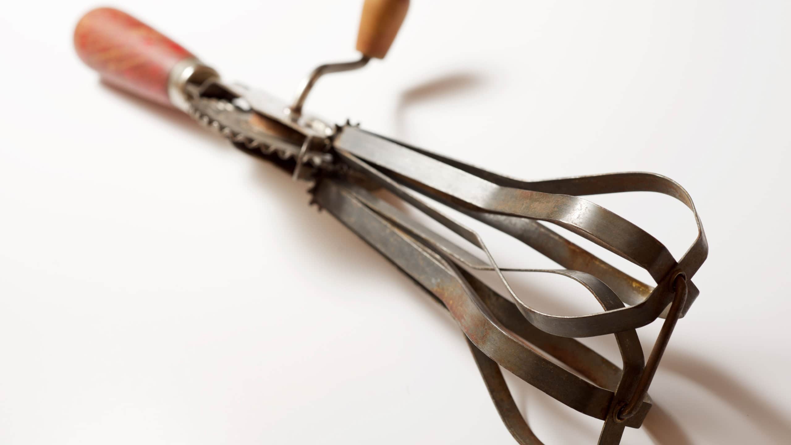 Old hand whisk on a white table.