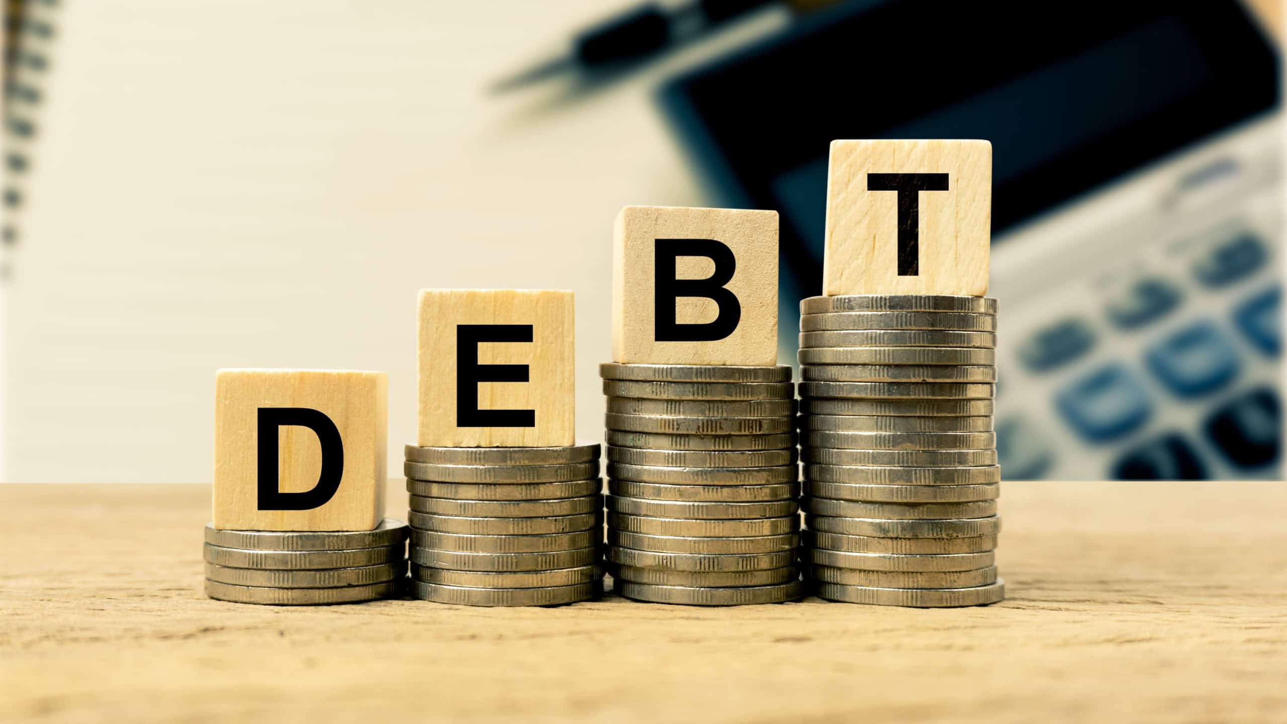 Concepts of liabilities and taxes that must be paid. A wooden block on stacked coins growth up on wood table with notebook and calculator as background. Depicts more debts that need to be paid.
