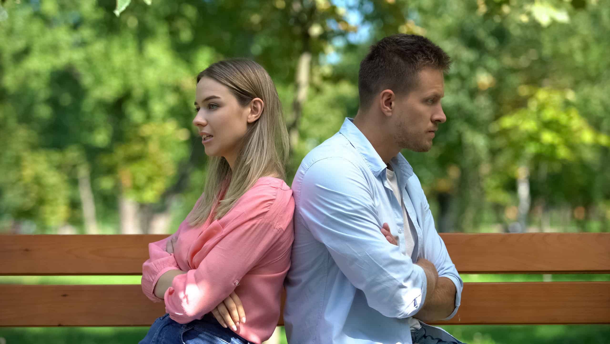 Upset couple sitting back on bench at park, communication crisis, conflict