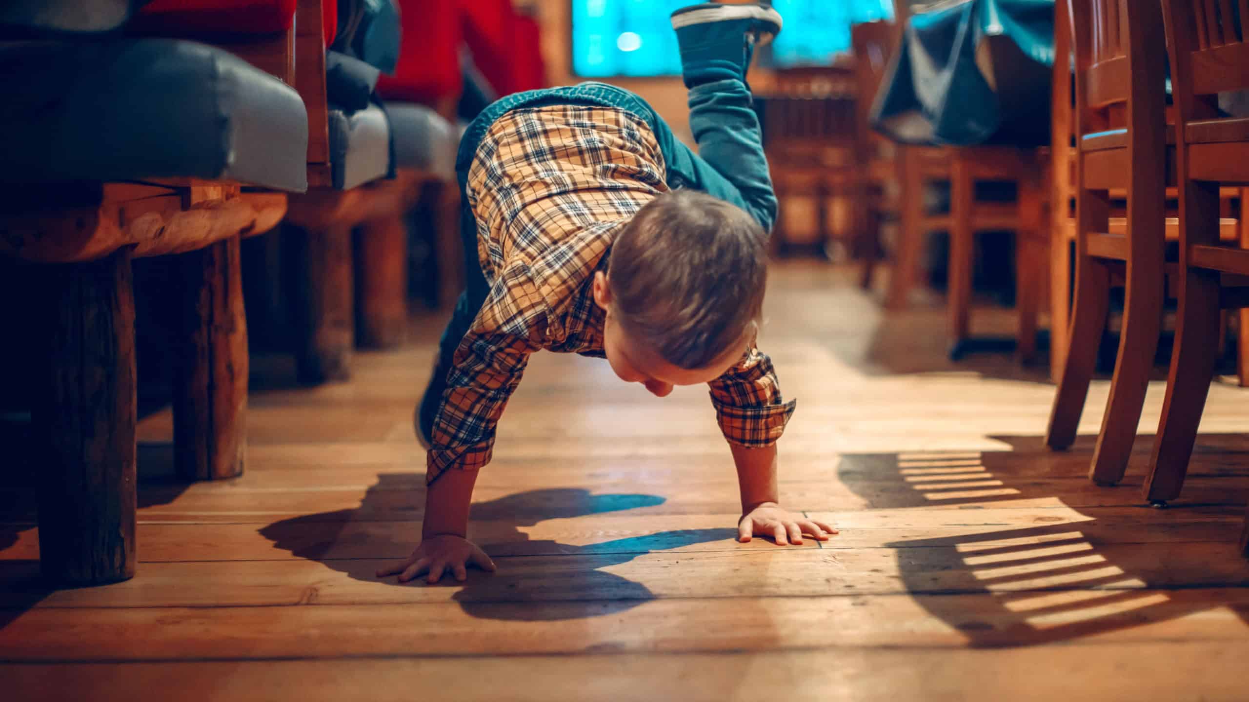 Cute adorable boy three years old having fun in cafe restaurant. Child playing on floor in public place. Freedom of self expression and behaviour for kids. Toddler touching dirty ground.