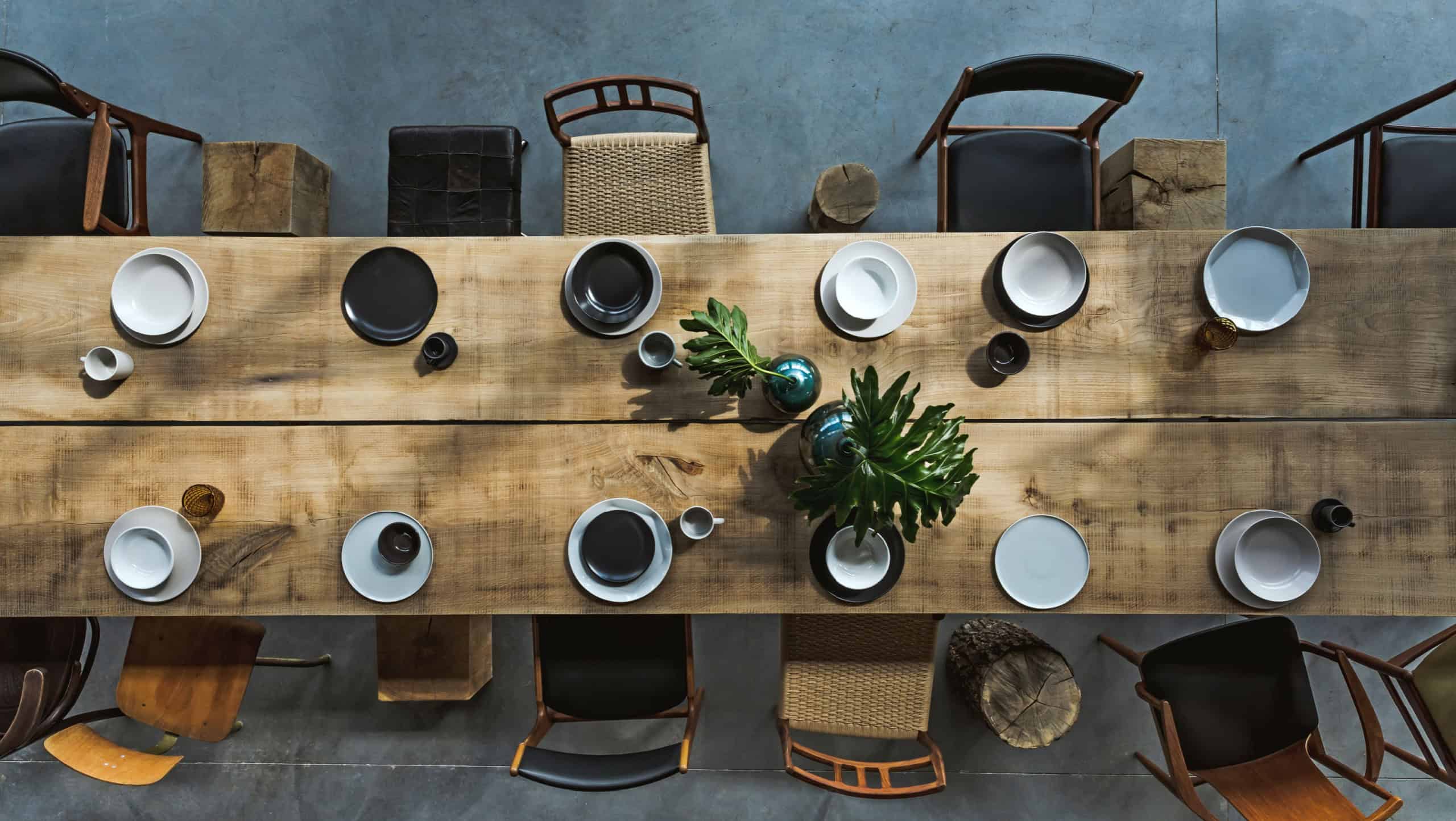 Stylish and modern interior design of conference room with design oak table, a lot of retro chairs, wooden cubes, plates and elegant accessories. Cement floor. Template. Office open space. Top view.