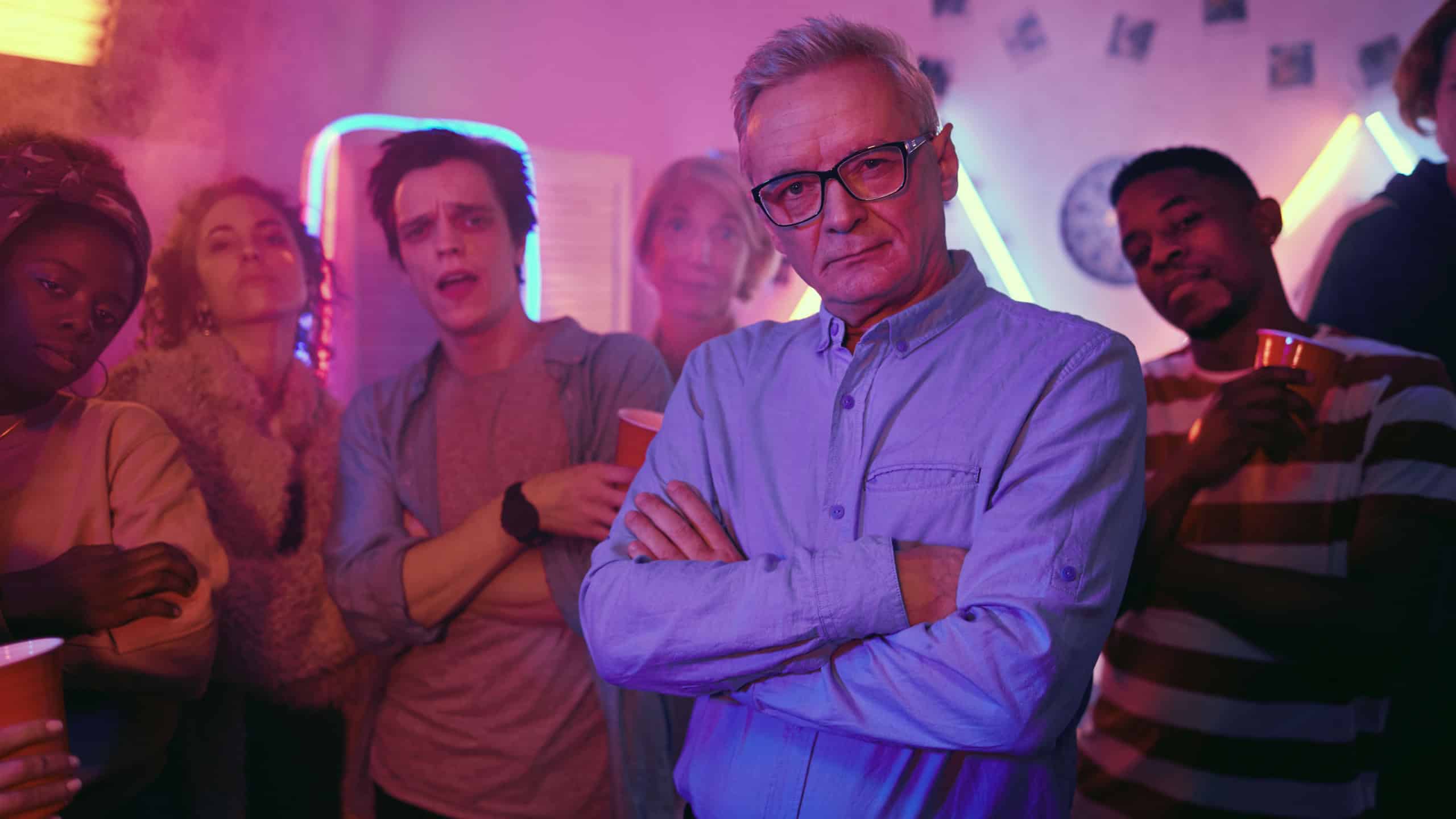 Portrait of senior man in eyeglasses standing with arms crossed and looking at camera while visiting party