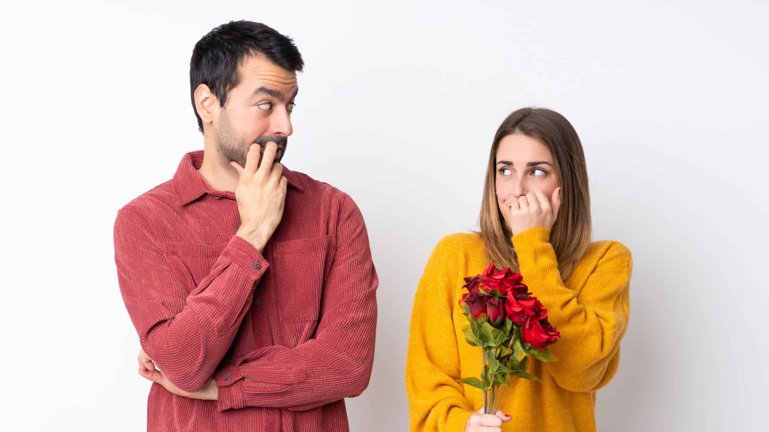 Couple in Valentine Day holding flowers over isolated background is a little bit nervous and scared putting hands to mouth