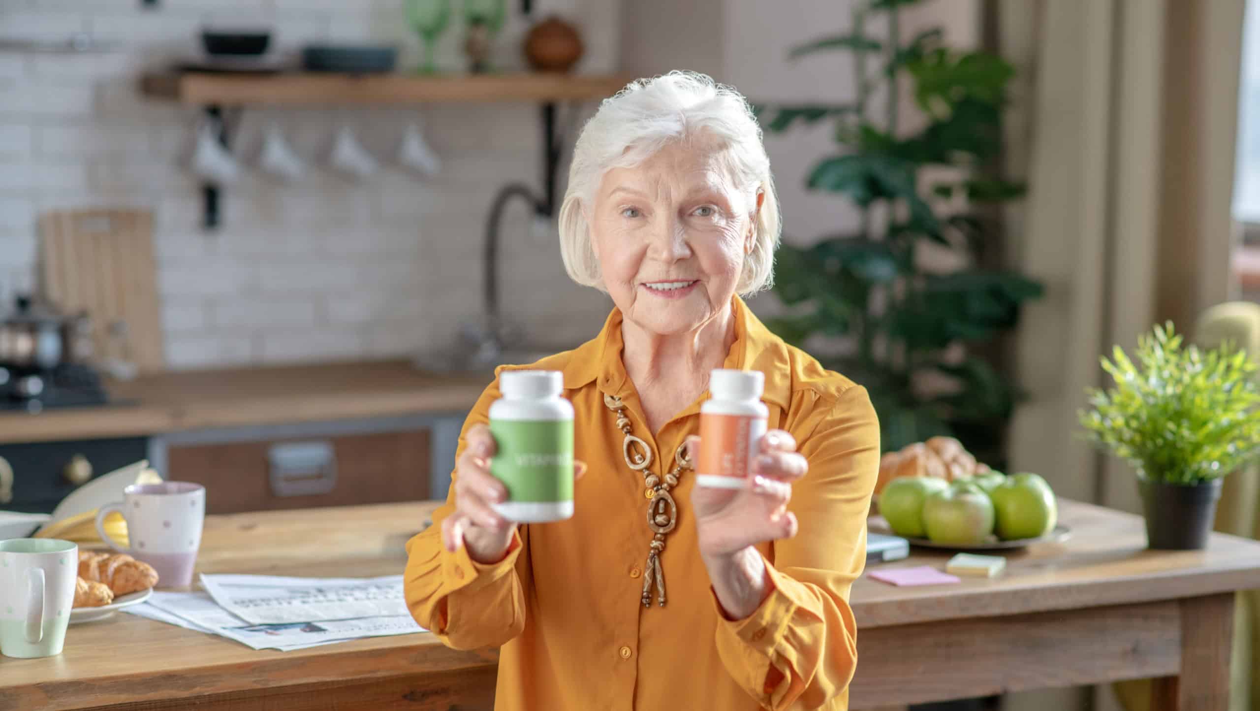 Be healthy. Grey-haired good-looking woman showing two jars with vitamins