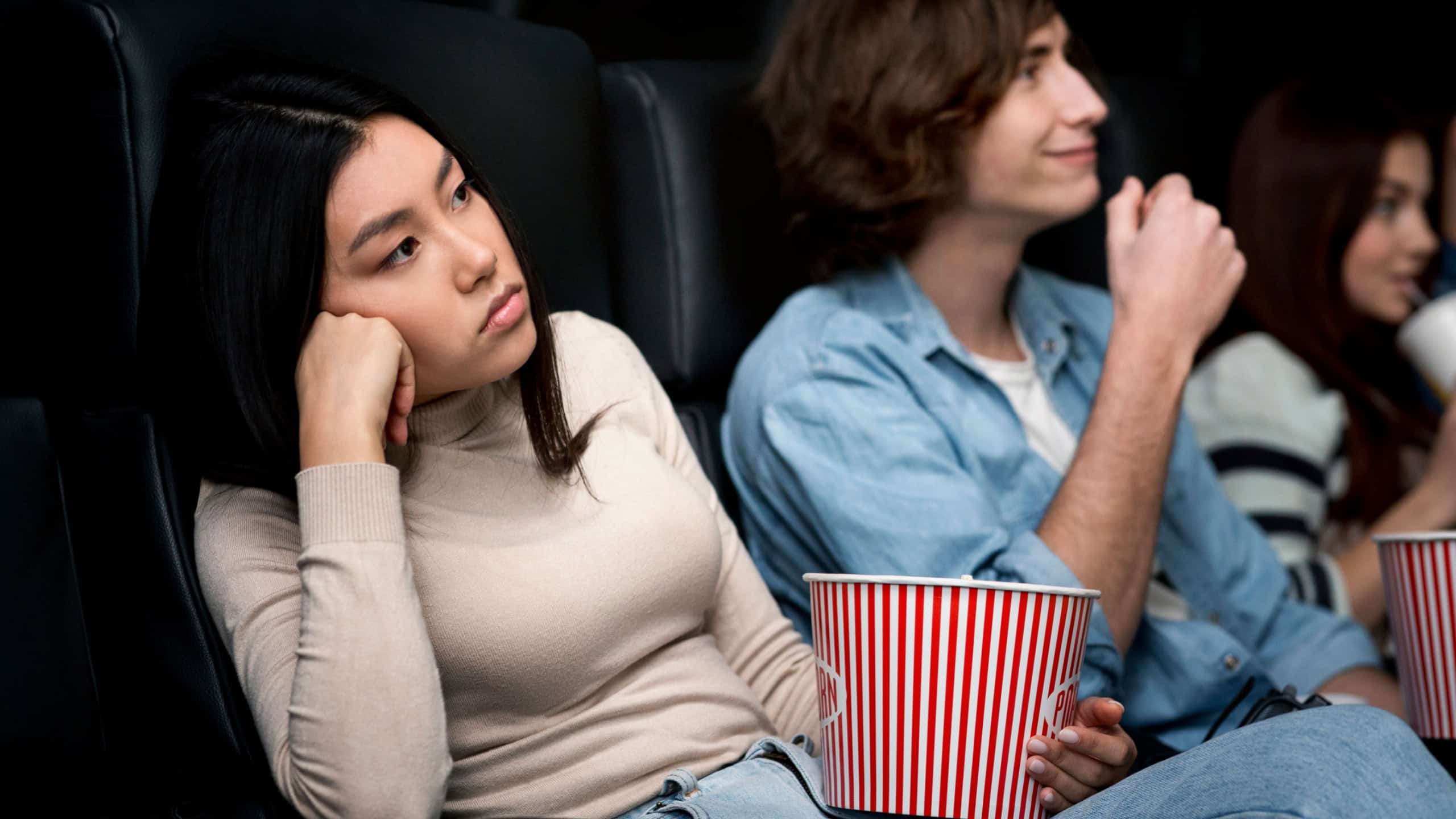 Dull date concept. Bored young lady with boyfriend watching movie in cinema