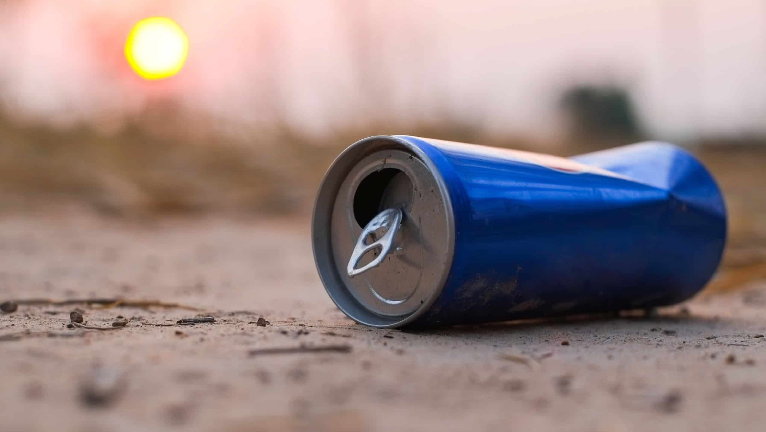 Garbage from blue aluminum cans that are thrown away on the ground which is a problem and pollution to the environment with sun light in evening close-up.