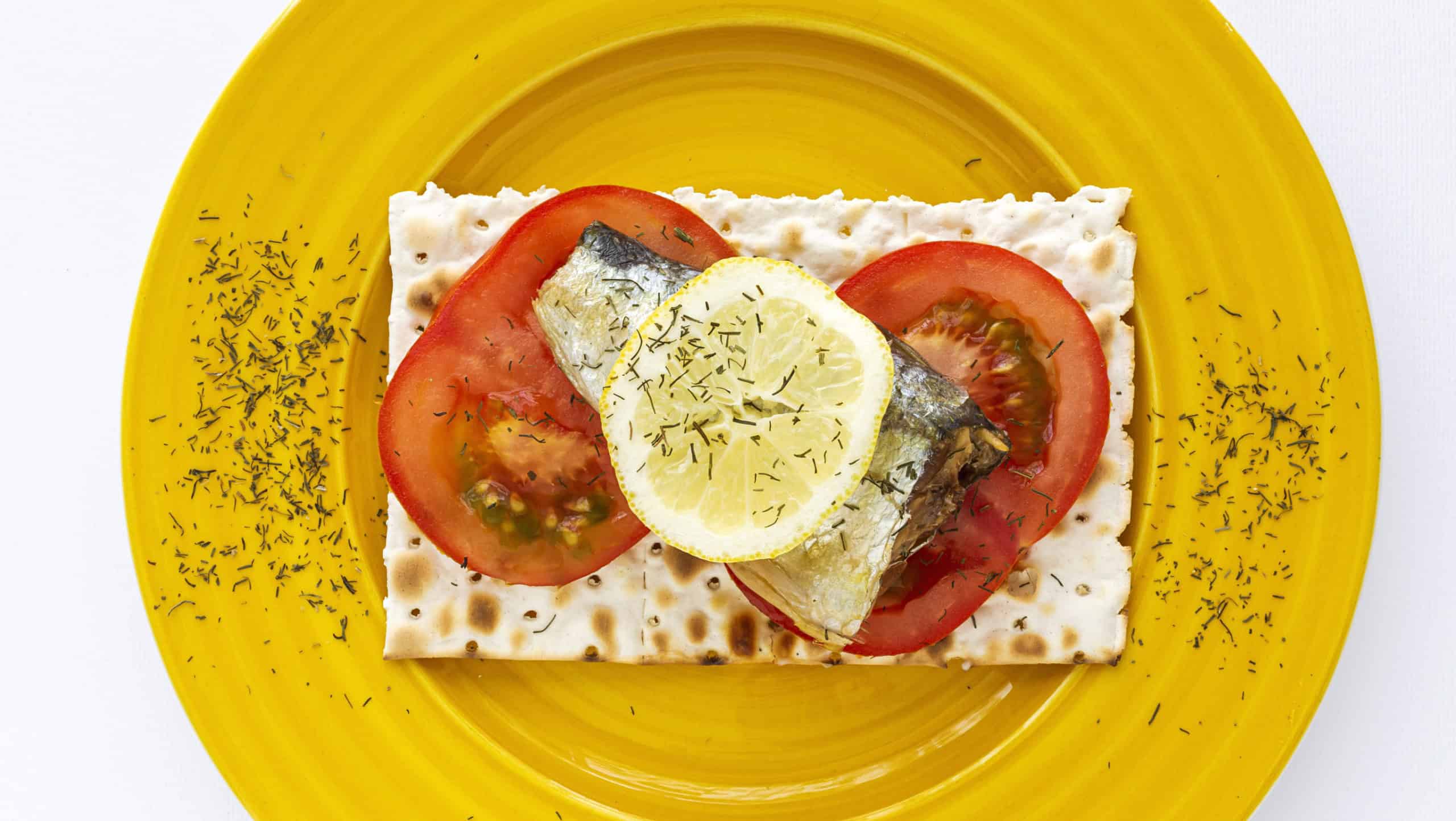 Salty crackers with sardine, tomato and lemon from above on colors background. Flat lay. Top view