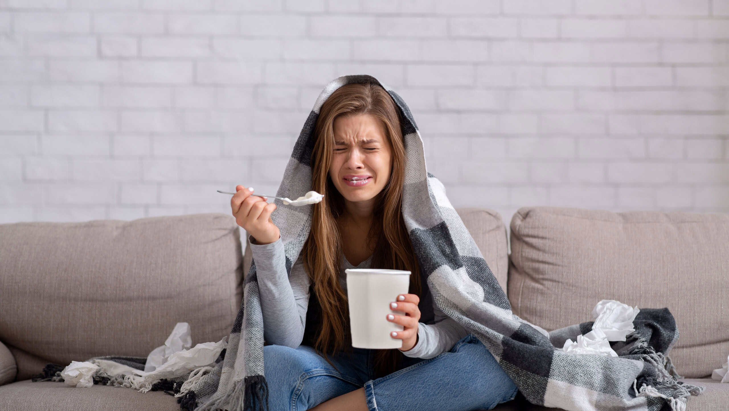 Heartbroken young woman eating ice cream from bucket while watching romantic movie on TV at home. Sad lady crying over breakup or relationship problems, feeling depressed and lonely