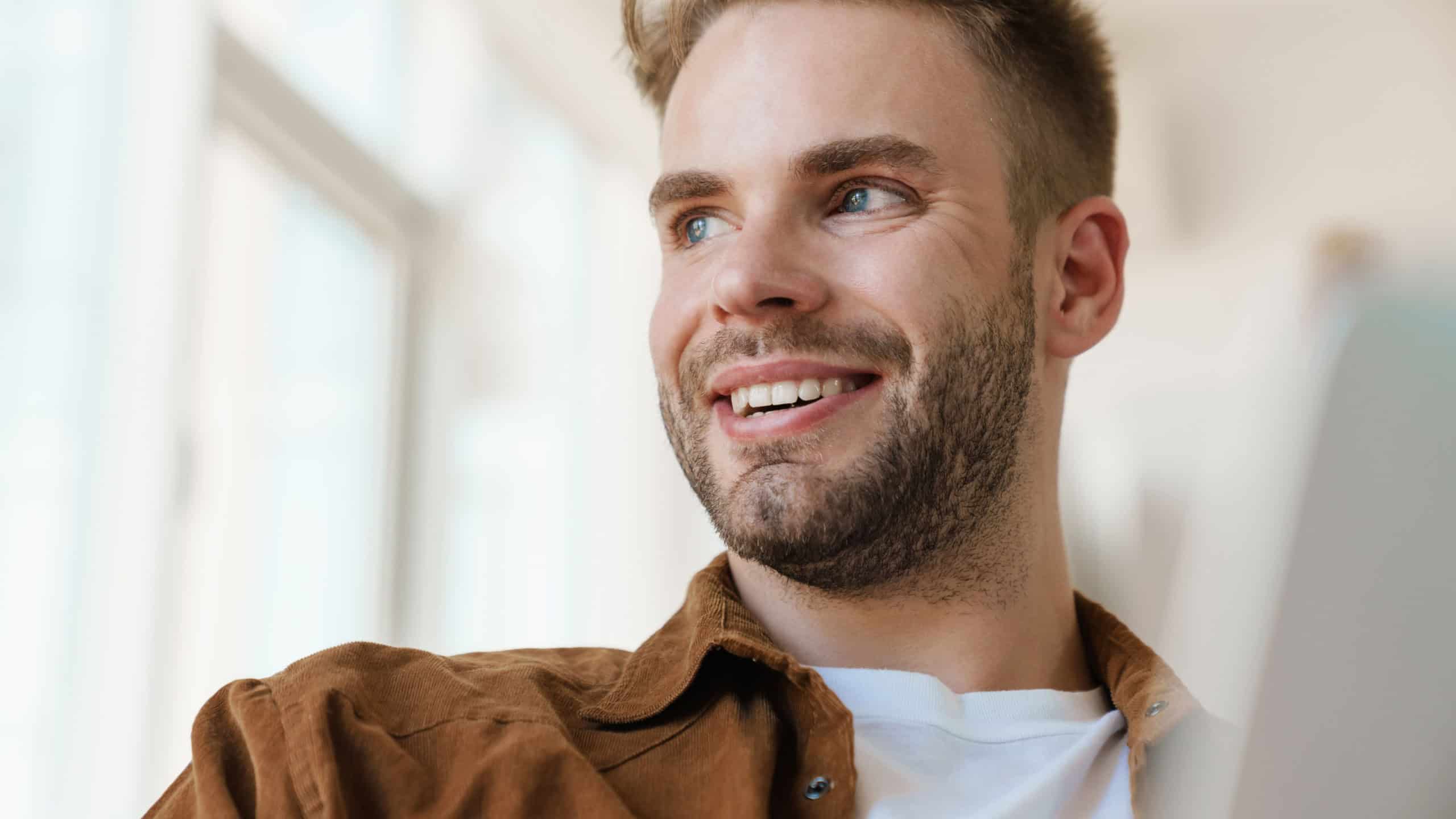 Handsome cheerful guy working with laptop and smiling at home
