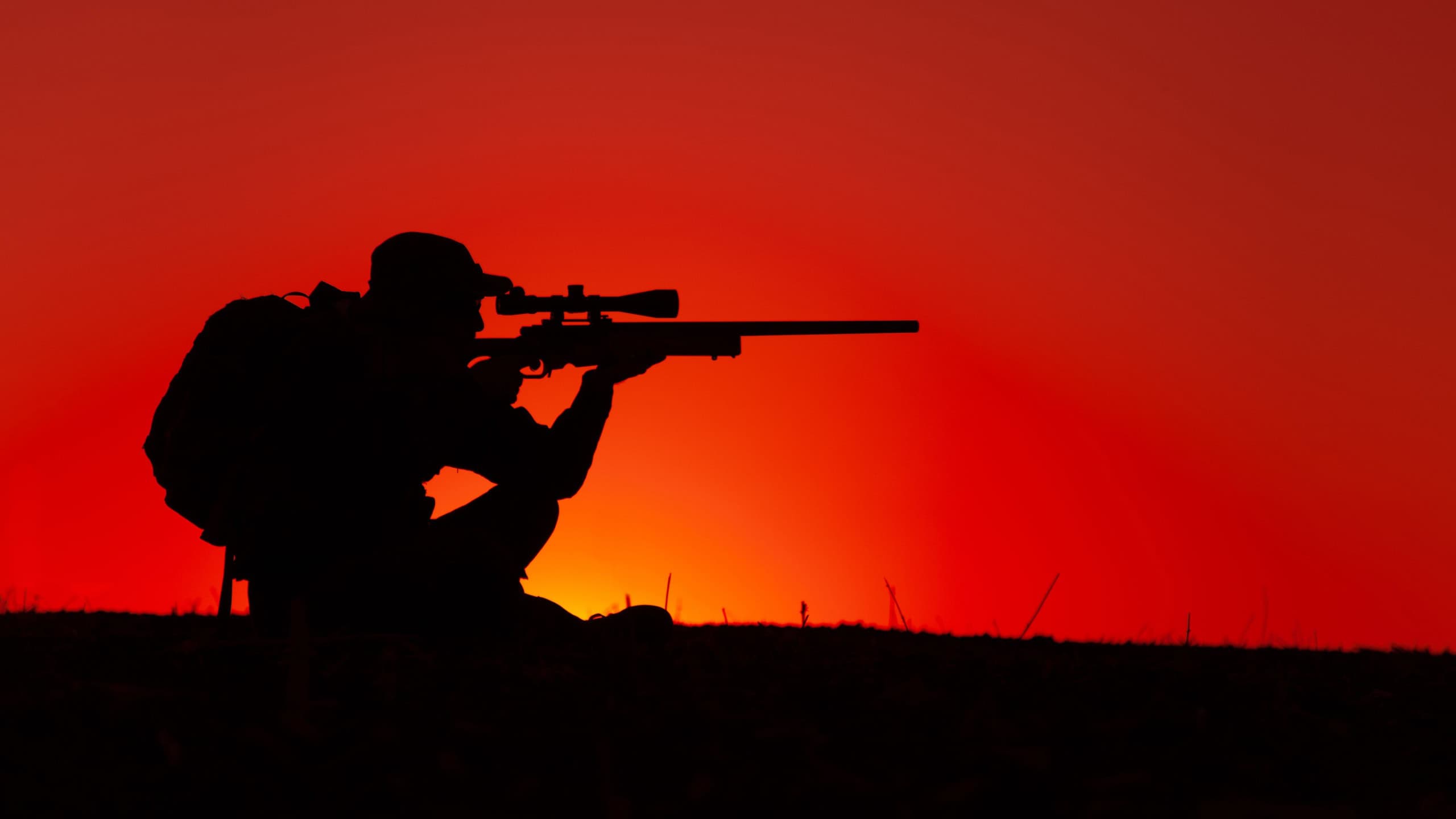 Commando team sniper, army special forces shooter aiming, shooting sniper rifle while sitting on sea or ocean shore during sunset. Coast or border guard soldier observing coastline with optical sight