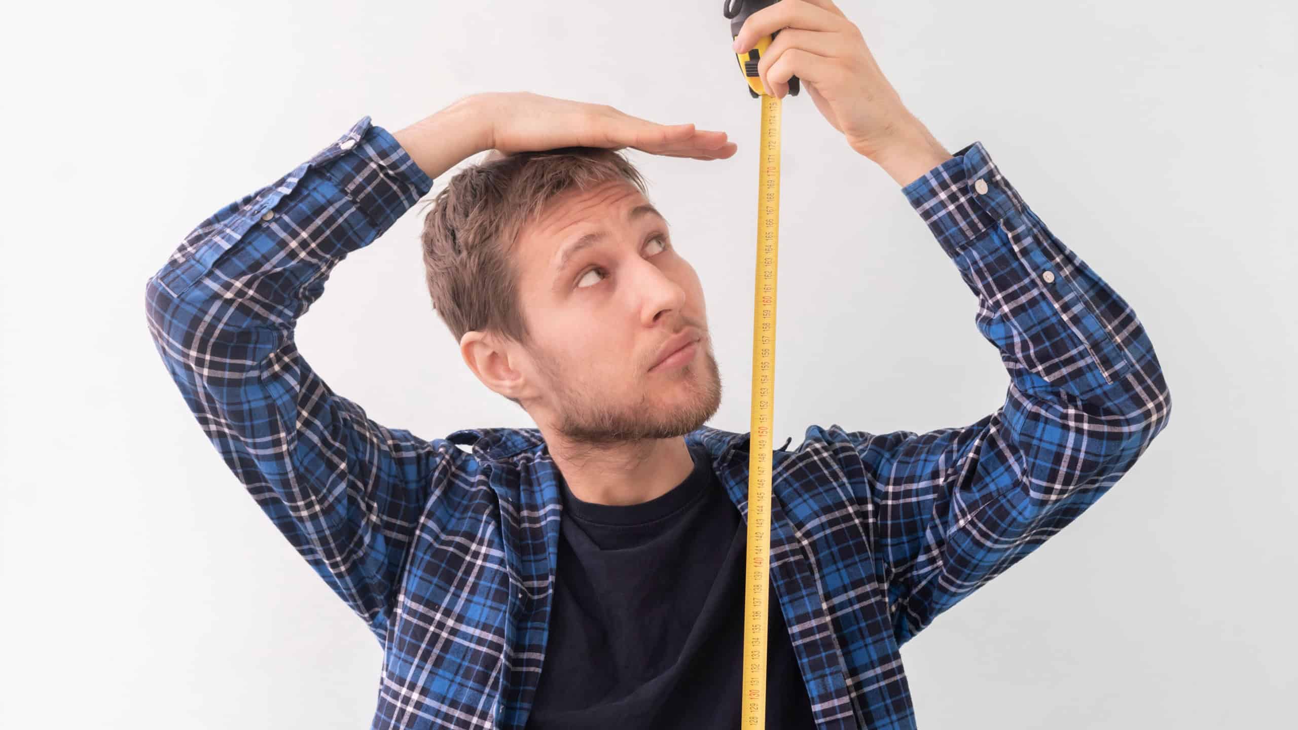 Simple adult male person with a roll tape measure the height against the wall