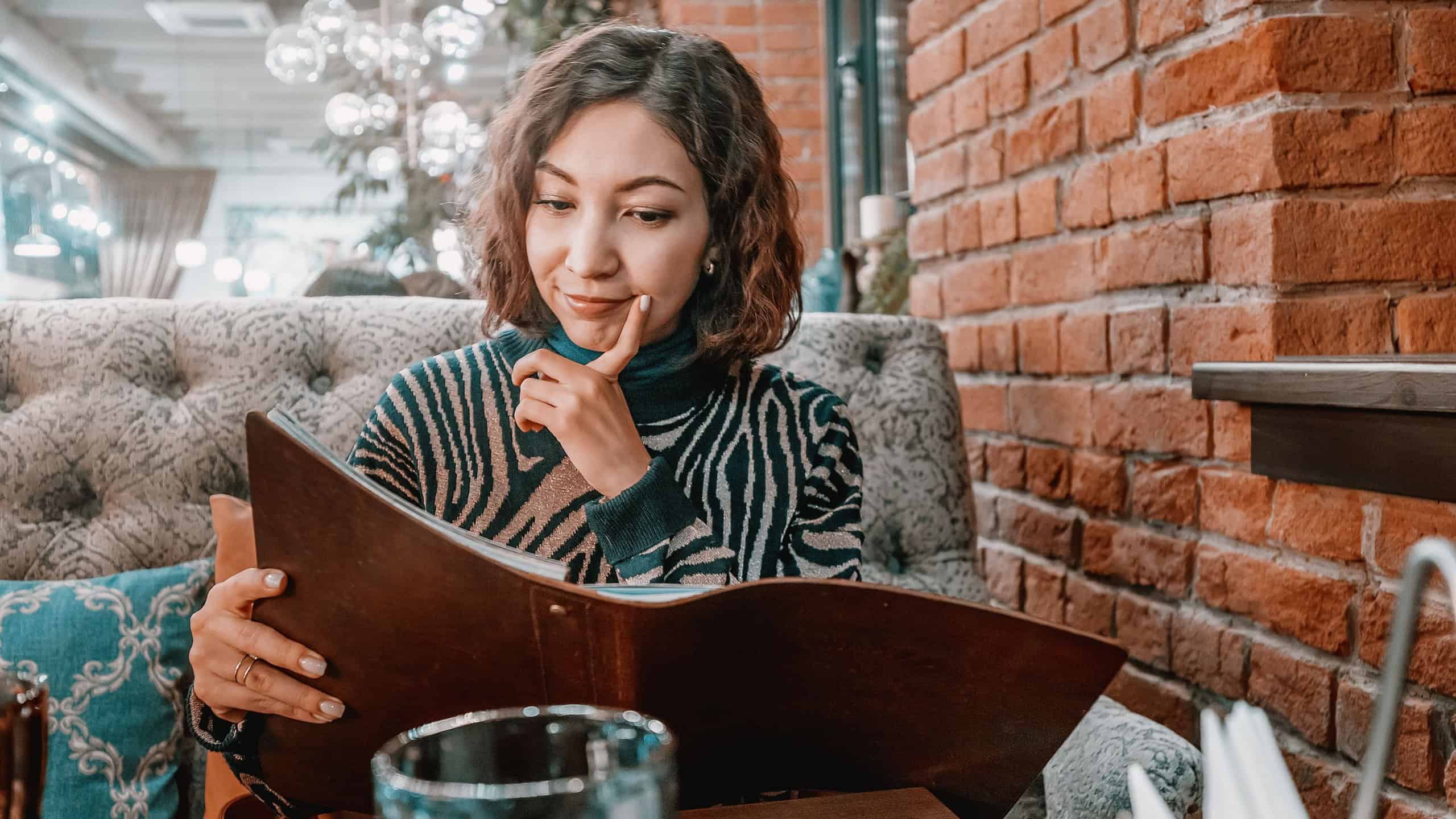 Happy woman chooses food and drinks from a large menu in a restaurant