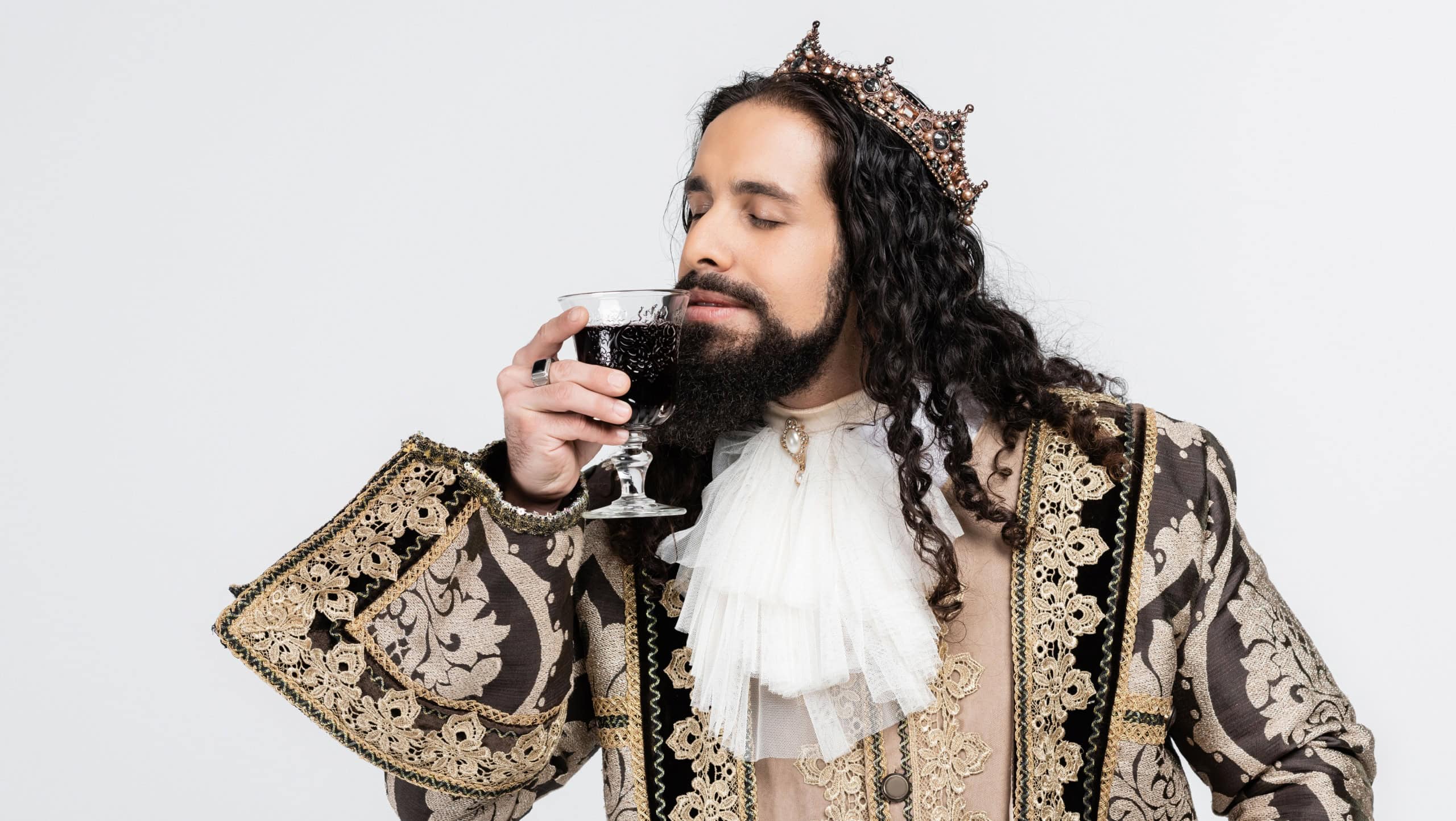 hispanic king in medieval clothing and crown smelling glass of red wine isolated on white