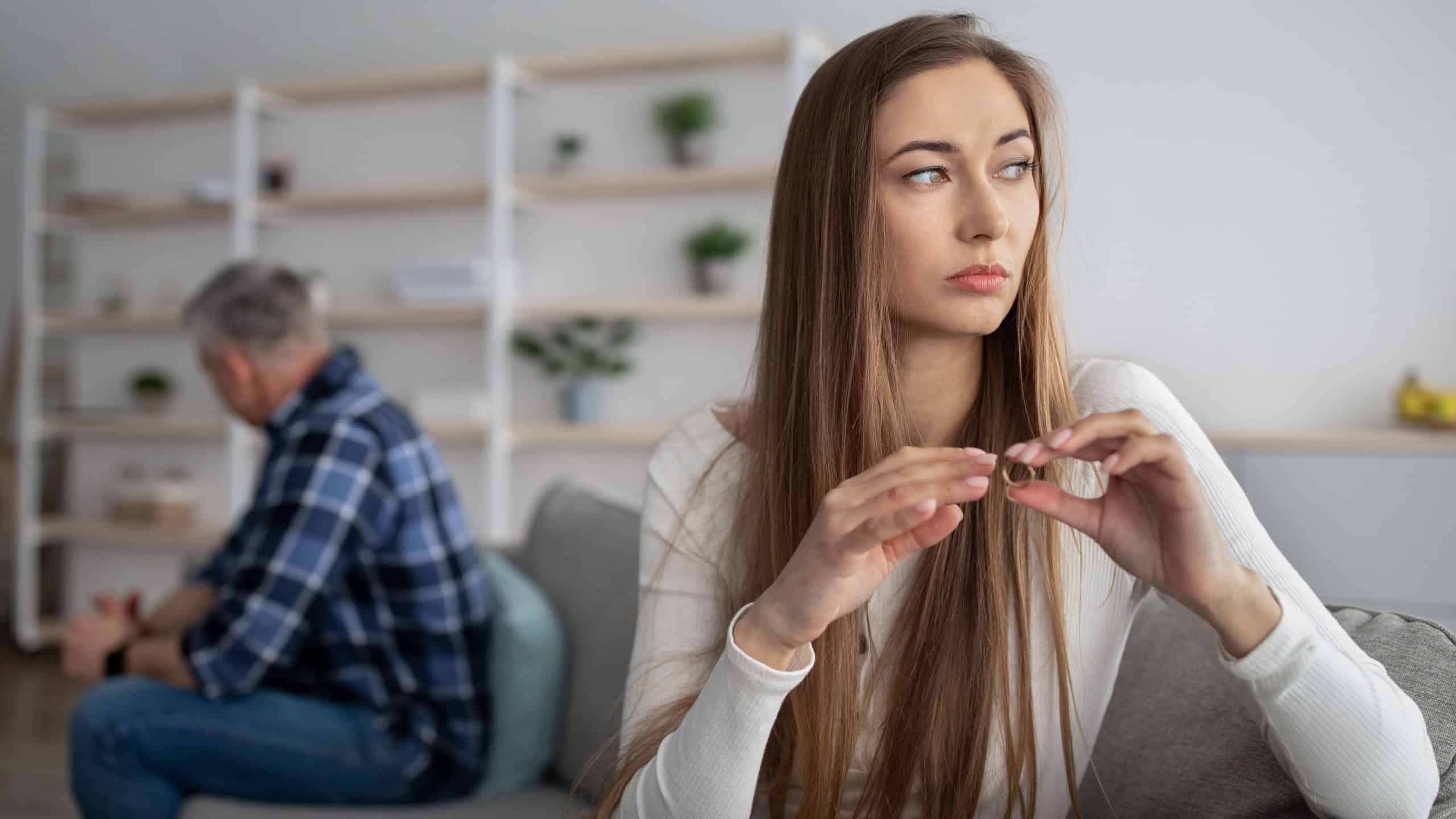 Unhappy mature woman taking off wedding ring, thinking about divorce with her husband indoors, free space. Middle-aged couple going through breakup or separation, having relationship problems