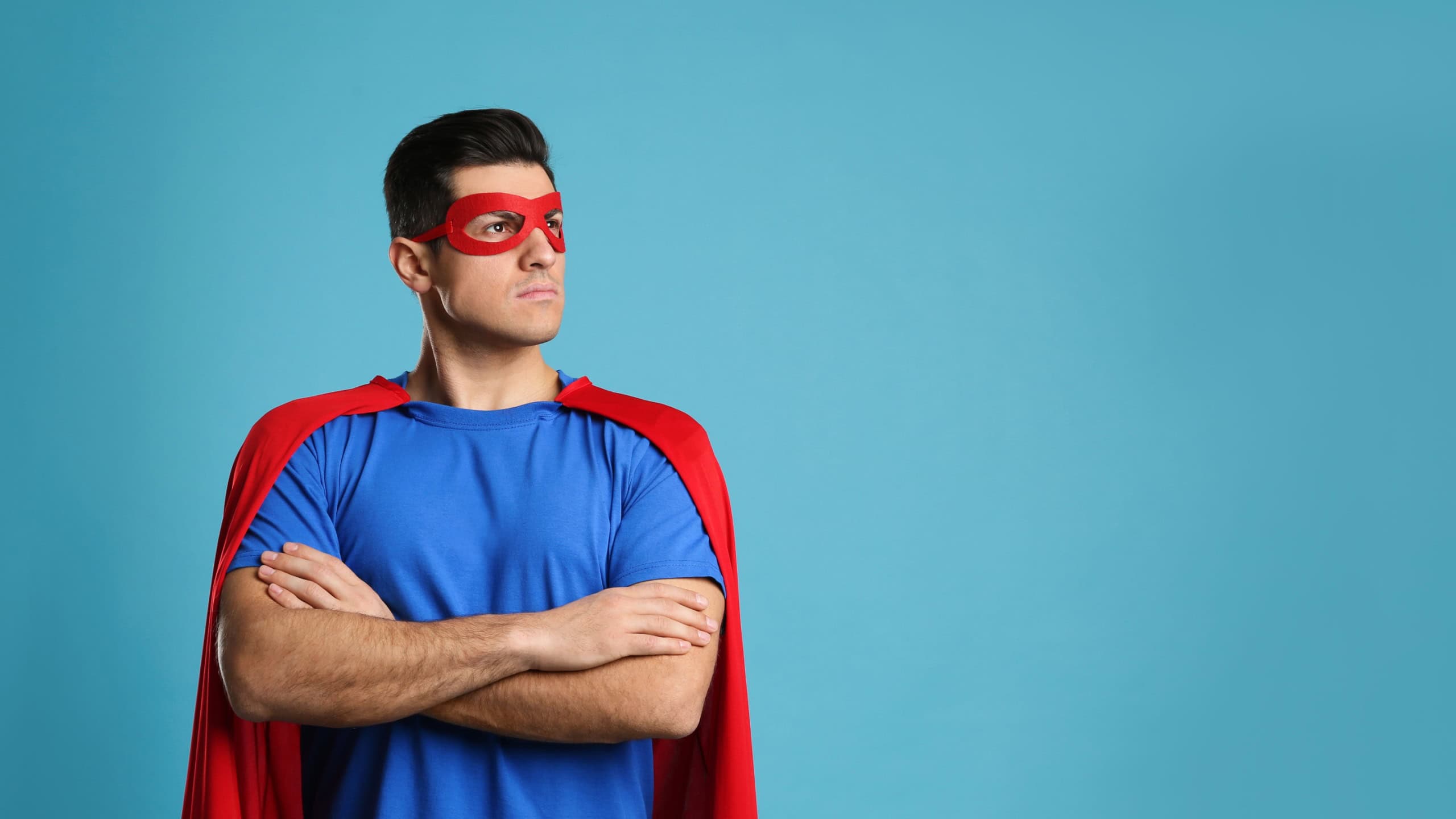 Man wearing superhero cape and mask on light blue background.