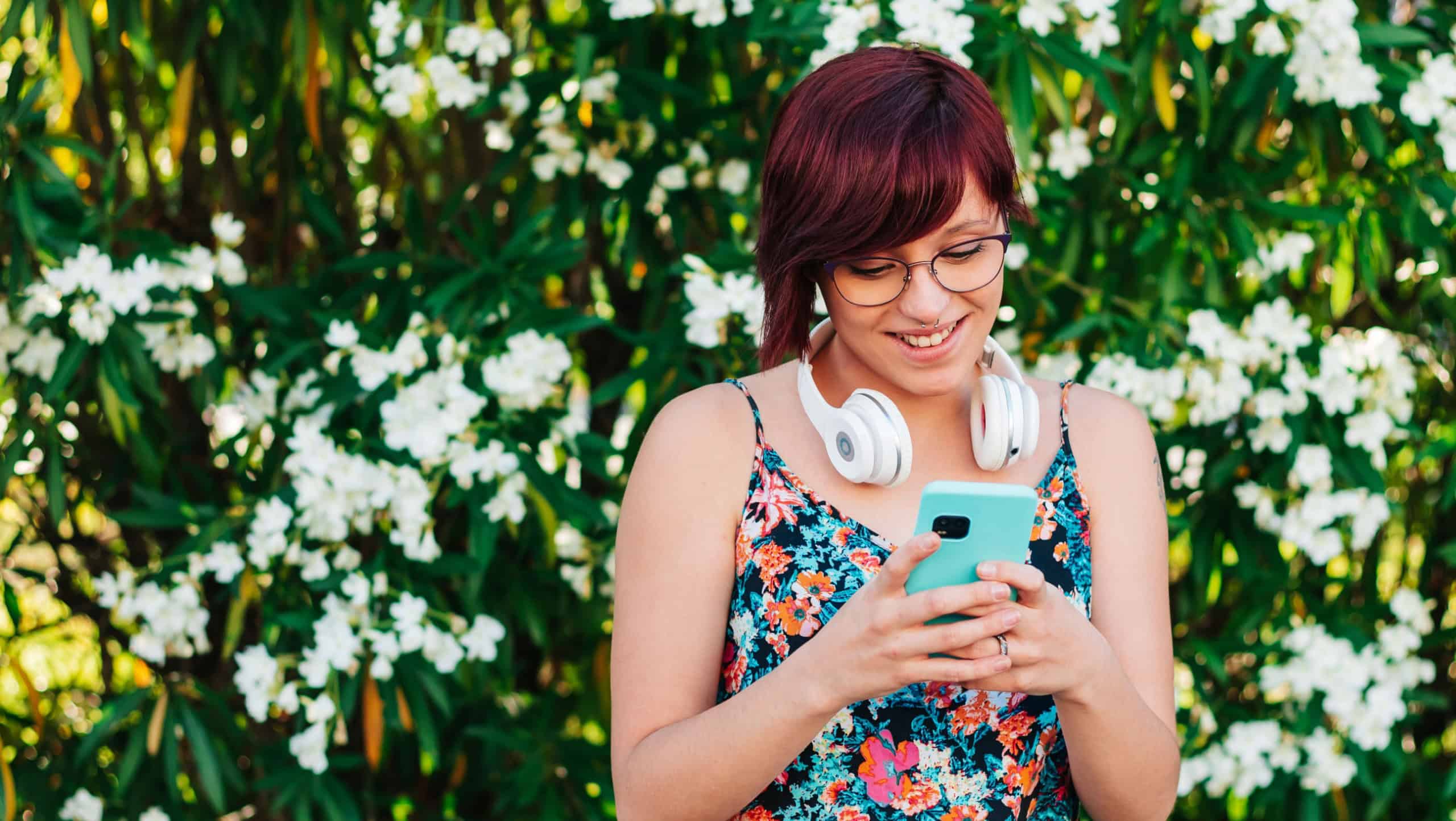 Young Caucasian woman and student with glasses and headphones, using their mobile phone outdoors. lifestyle and social media concept.