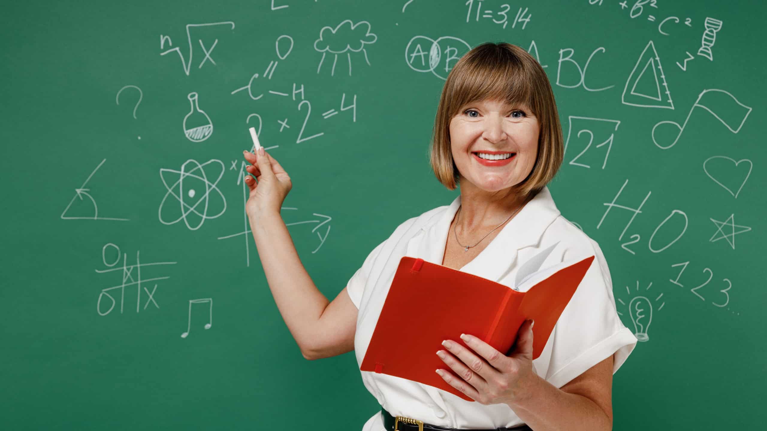 Happy clever vivid teacher mature elderly lady woman 55 wear white shirt hold in hand open book point with chalk isolated on green wall blackboard background studio. Education in high school concept