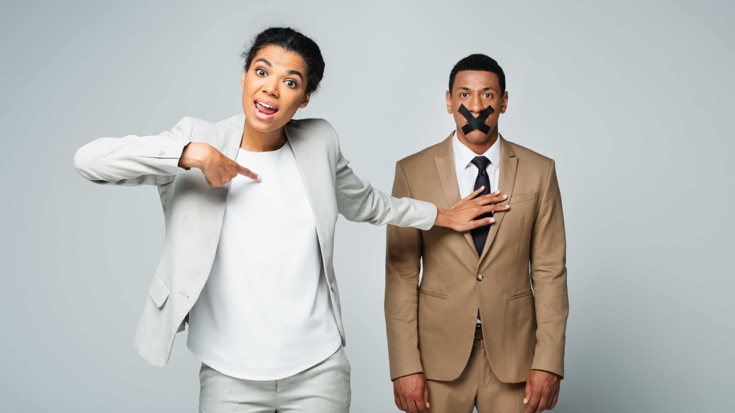 Arrogant african american businesswoman pointing at herself and pushing away manager with scotch tape on mouth isolated on grey