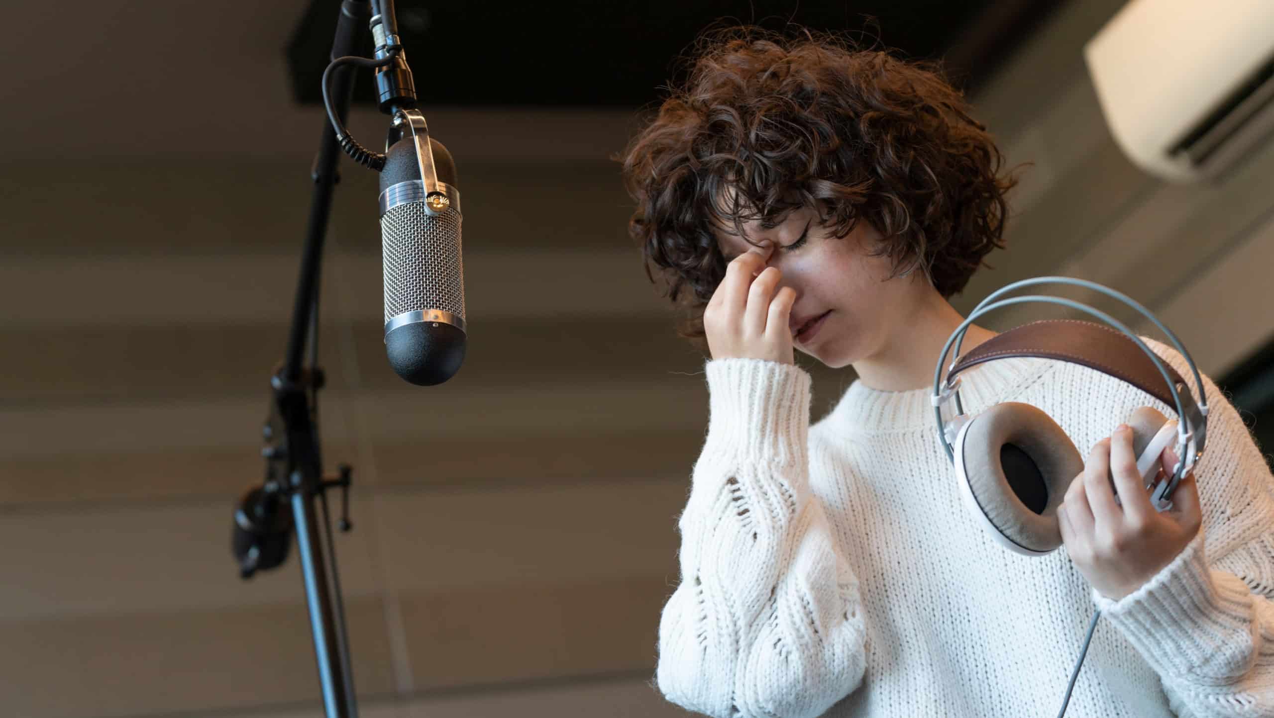 A young curly hair singer woman with a headache recording a song in a studio