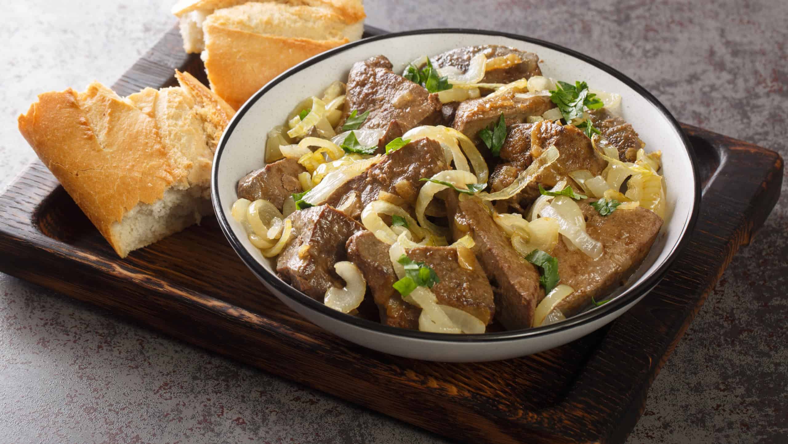 Homemade food fried beef liver with onions and herbs close-up in a plate and bread on a wooden tray on the table. horizontal