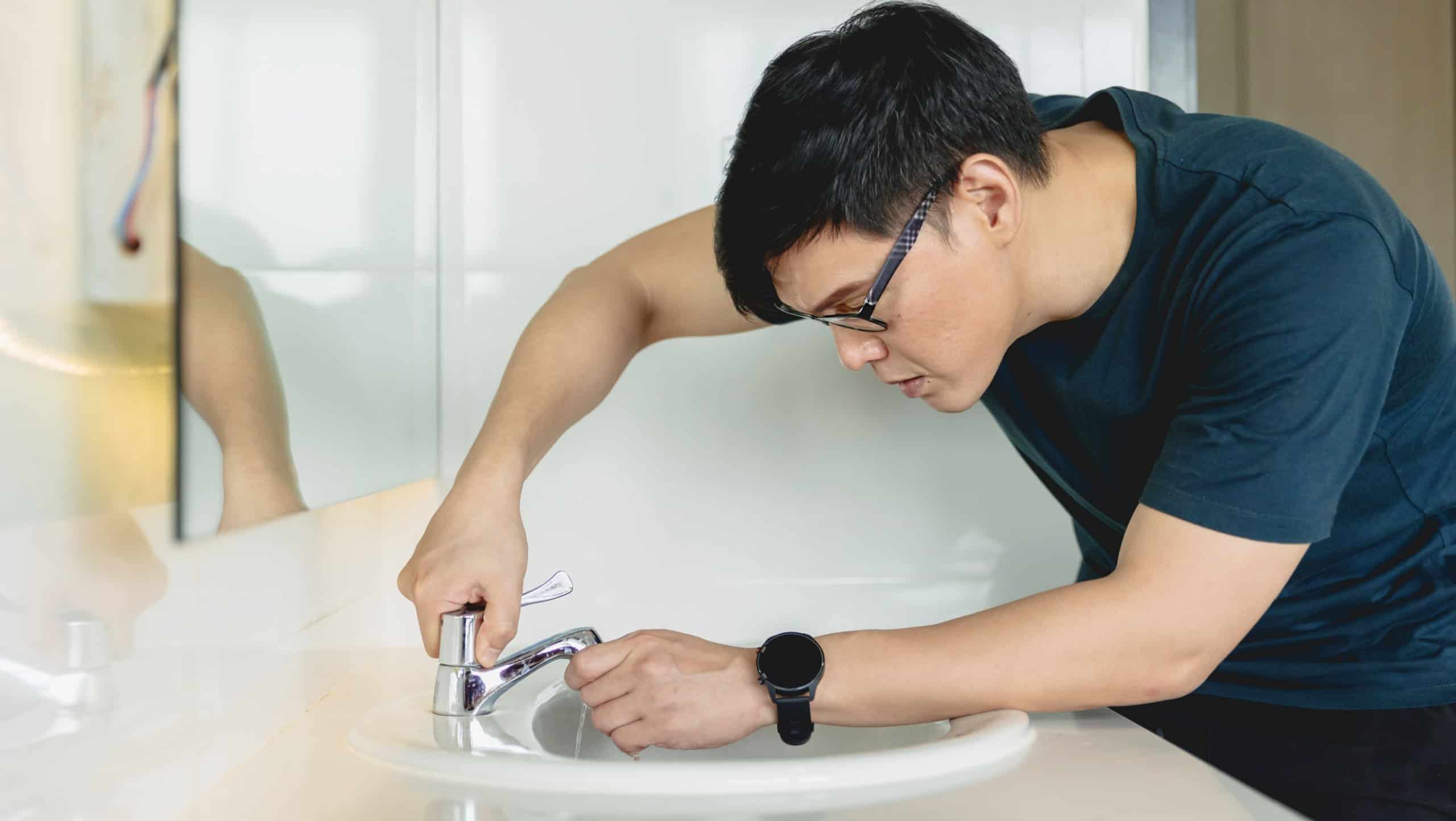 Asian male repair sink faucet pipe leak. man working as handyman in home.