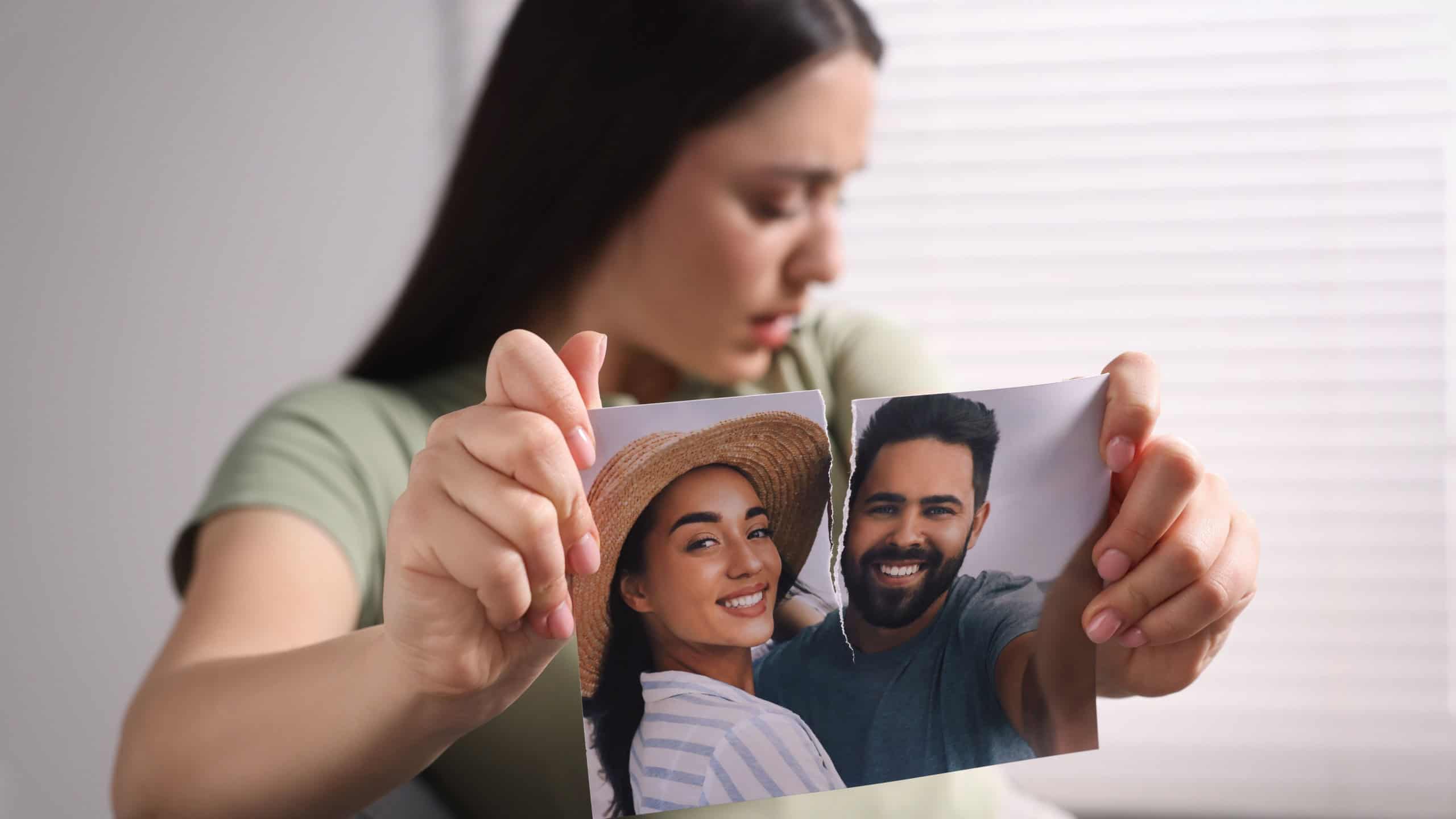 Upset woman ripping photo indoors, focus on picture. Divorce concept