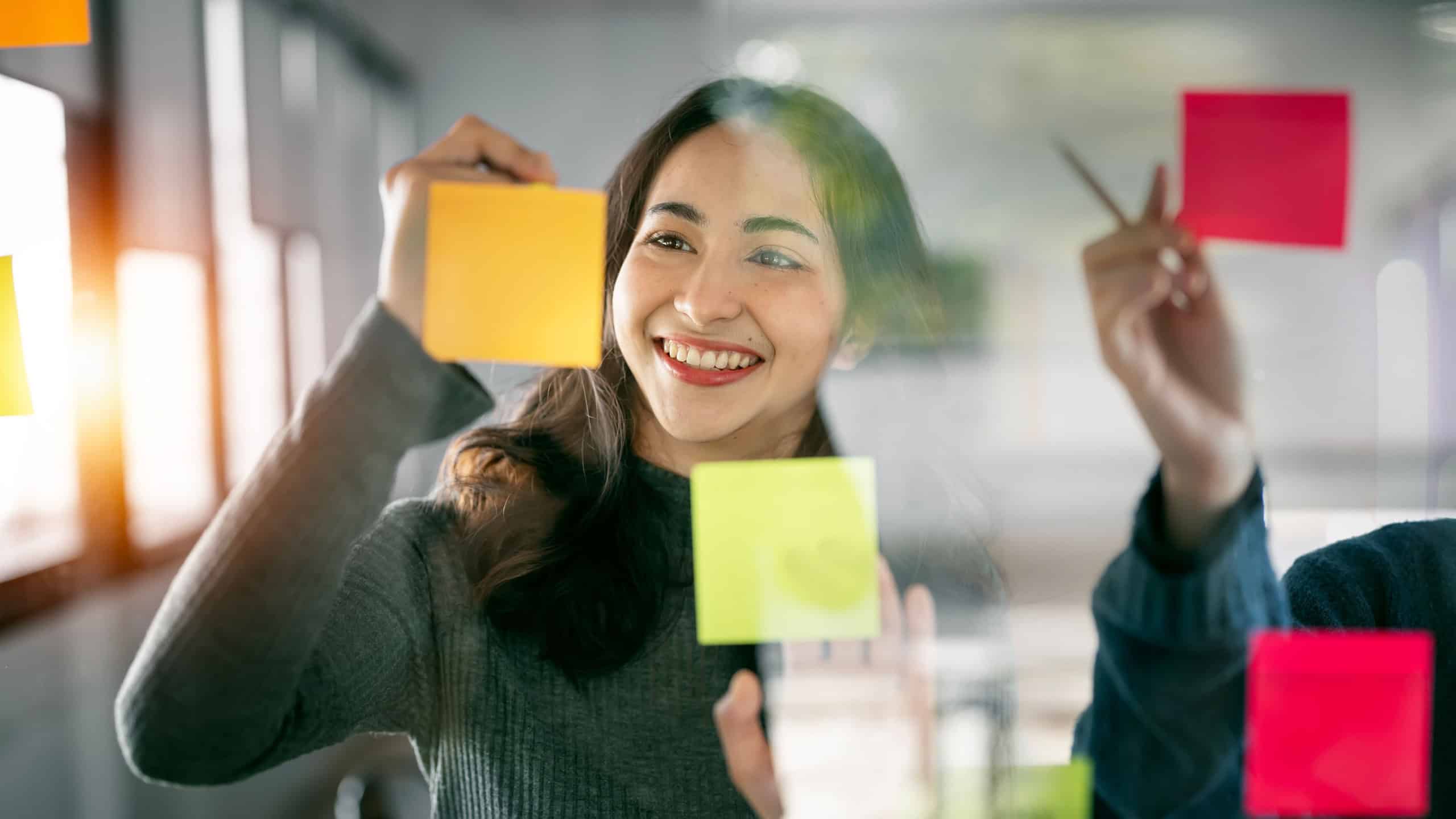 Young businesswoman creative team using post it notes in glass wall to writing strategy business plan to development grow to success.